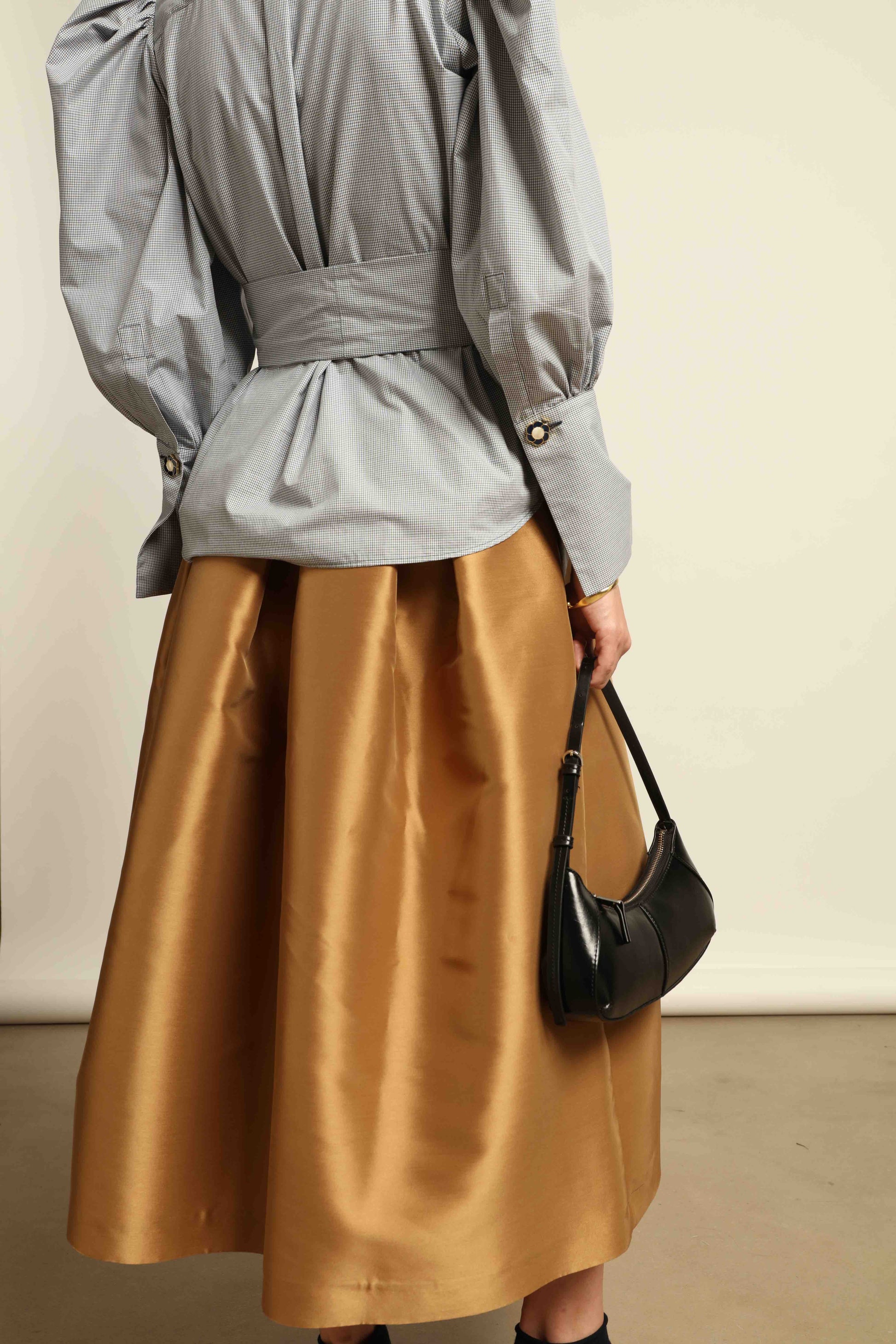 Model is wearing Duchesse Camel Skirt by Lunatica Milano, part of House of Woven Stories selection. Flowing pleated maxi skirt crafted from a sumptuous soft-blend fabric. Timelessly elegant, feminine, and handmade in Italy.