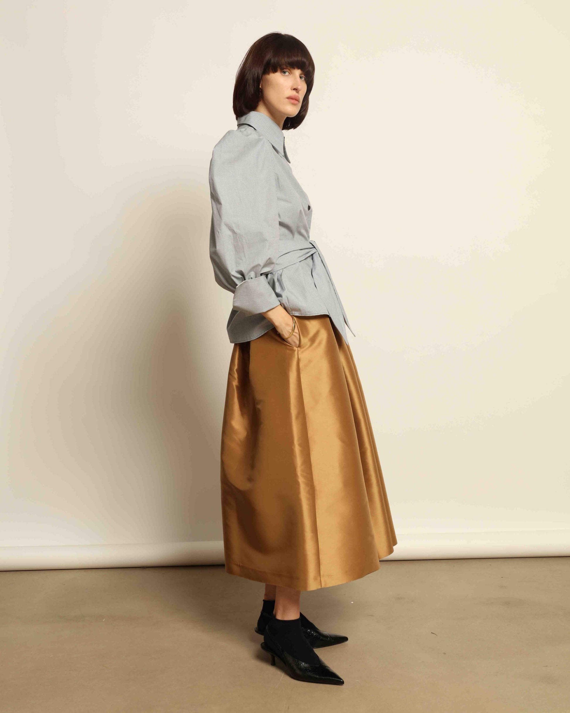 Model is wearing Duchesse Camel Skirt by Lunatica Milano, part of House of Woven Stories selection. Flowing pleated maxi skirt crafted from a sumptuous soft-blend fabric. Timelessly elegant, feminine, and handmade in Italy.