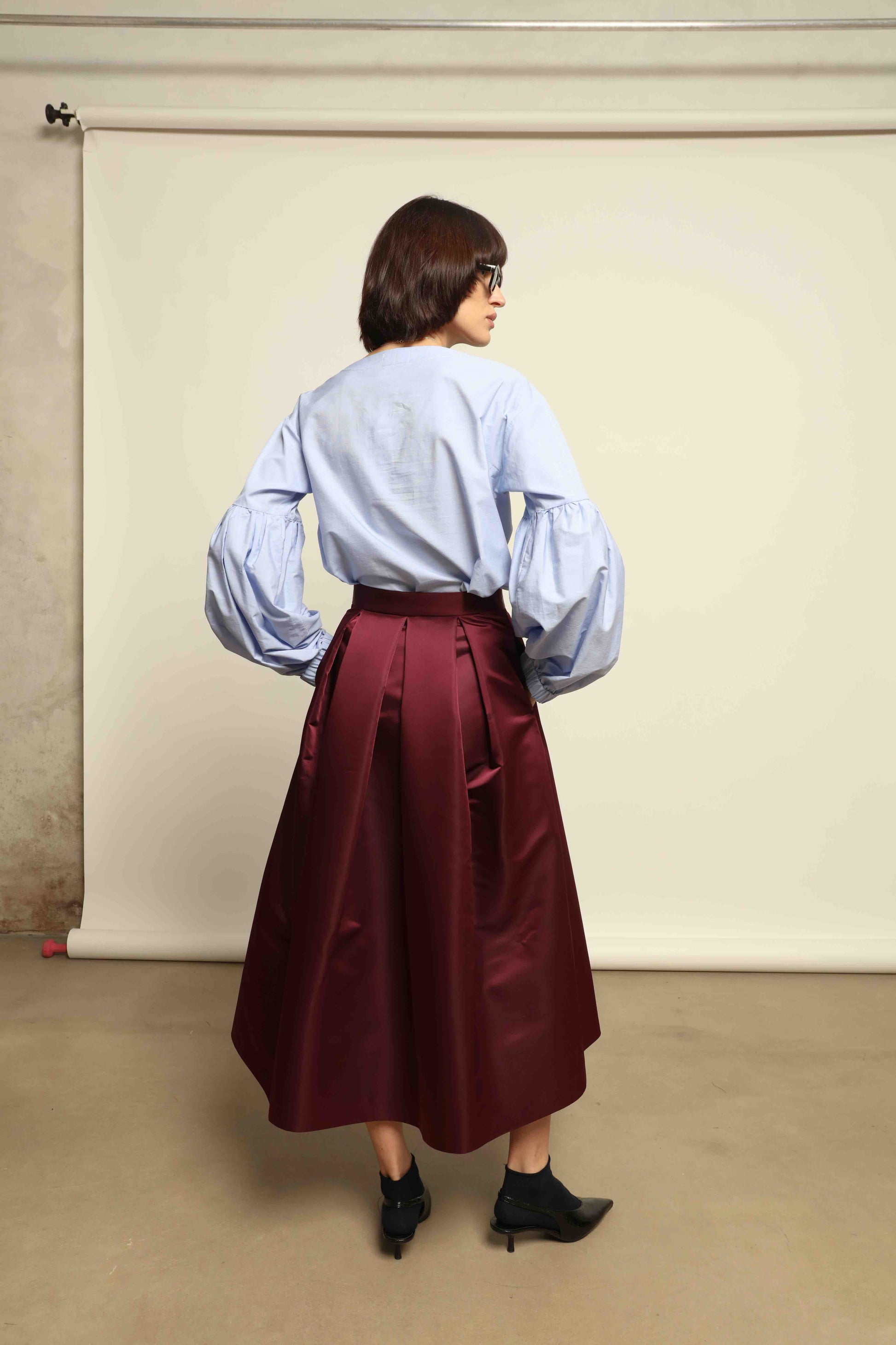 Model is wearing the Duchesse Violet Skirt by Lunatica Milano in mirtillo purple with box pleats and a flowing, elegant silhouette.
