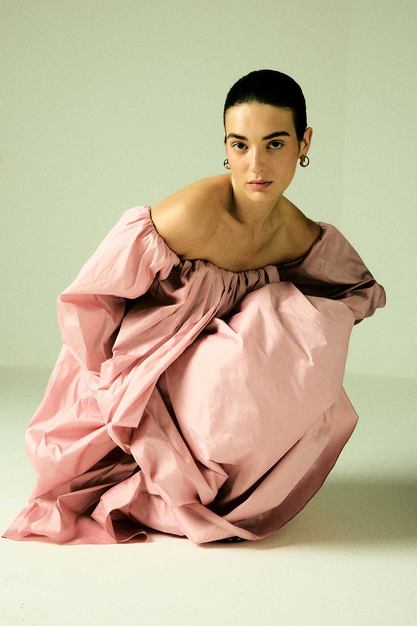 Model wearing a pink Eleanor maxi dress by Abadia from the House of Nomad Stories collection, featuring an off-shoulder neckline, corset bodice, and voluminous gathered skirt with a sculptural fluid silhouette.
