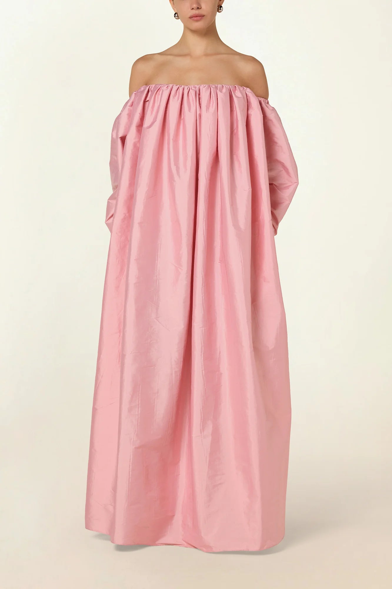 Model wearing a pink Eleanor maxi dress by Abadia from the House of Nomad Stories collection, featuring an off-shoulder neckline, corset bodice, and voluminous gathered skirt with a sculptural fluid silhouette.