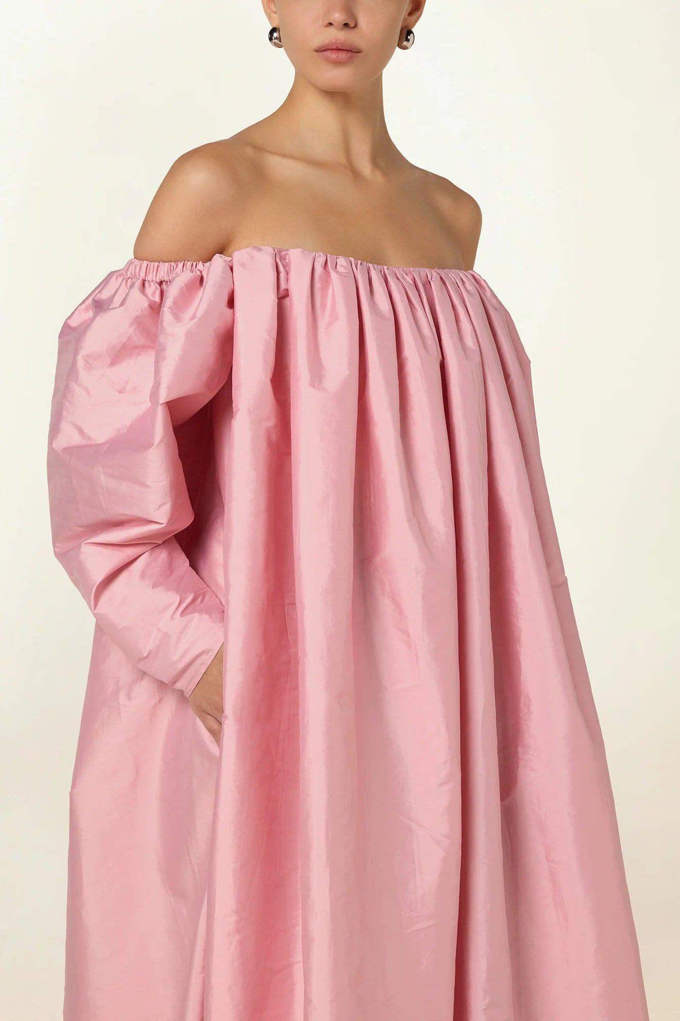 Model wearing a pink Eleanor maxi dress by Abadia from the House of Nomad Stories collection, featuring an off-shoulder neckline, corset bodice, and voluminous gathered skirt with a sculptural fluid silhouette.