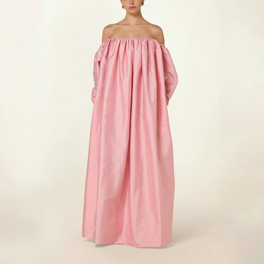 Model wearing a pink Eleanor maxi dress by Abadia from the House of Nomad Stories collection, featuring an off-shoulder neckline, corset bodice, and voluminous gathered skirt with a sculptural fluid silhouette.