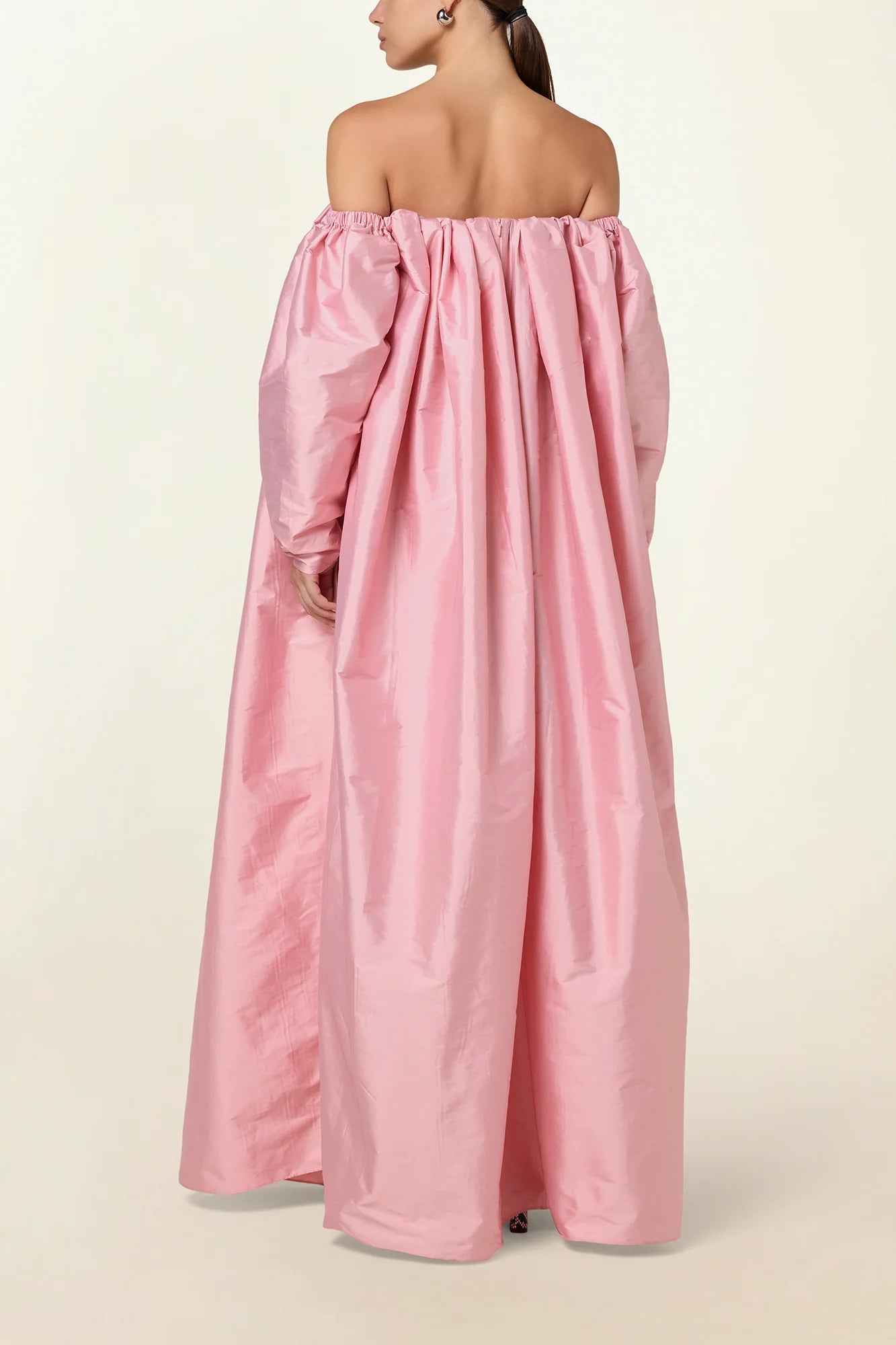 Model wearing a pink Eleanor maxi dress by Abadia from the House of Nomad Stories collection, featuring an off-shoulder neckline, corset bodice, and voluminous gathered skirt with a sculptural fluid silhouette.