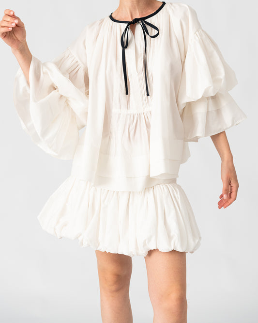 Model is wearing the Favignana Cotton and Silk Blouse by Les Vacances d’Irina, a vintage-inspired handmade blouse with pleated three-quarter sleeves, black bow neckline, and luxurious cotton-silk fabric, available at House of Woven Stories.