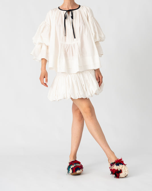 Model is wearing the Favignana Cotton and Silk Blouse by Les Vacances d’Irina, a vintage-inspired handmade blouse with pleated three-quarter sleeves, black bow neckline, and luxurious cotton-silk fabric, available at House of Woven Stories.
