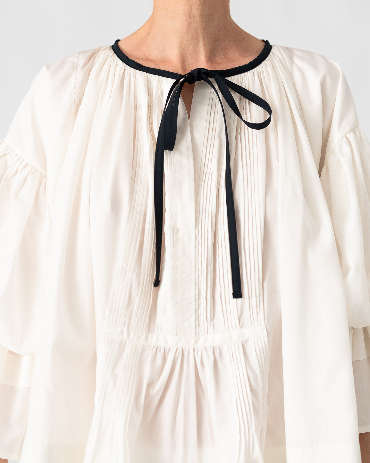 Model is wearing the Favignana Cotton and Silk Blouse by Les Vacances d’Irina, a vintage-inspired handmade blouse with pleated three-quarter sleeves, black bow neckline, and luxurious cotton-silk fabric, available at House of Woven Stories.