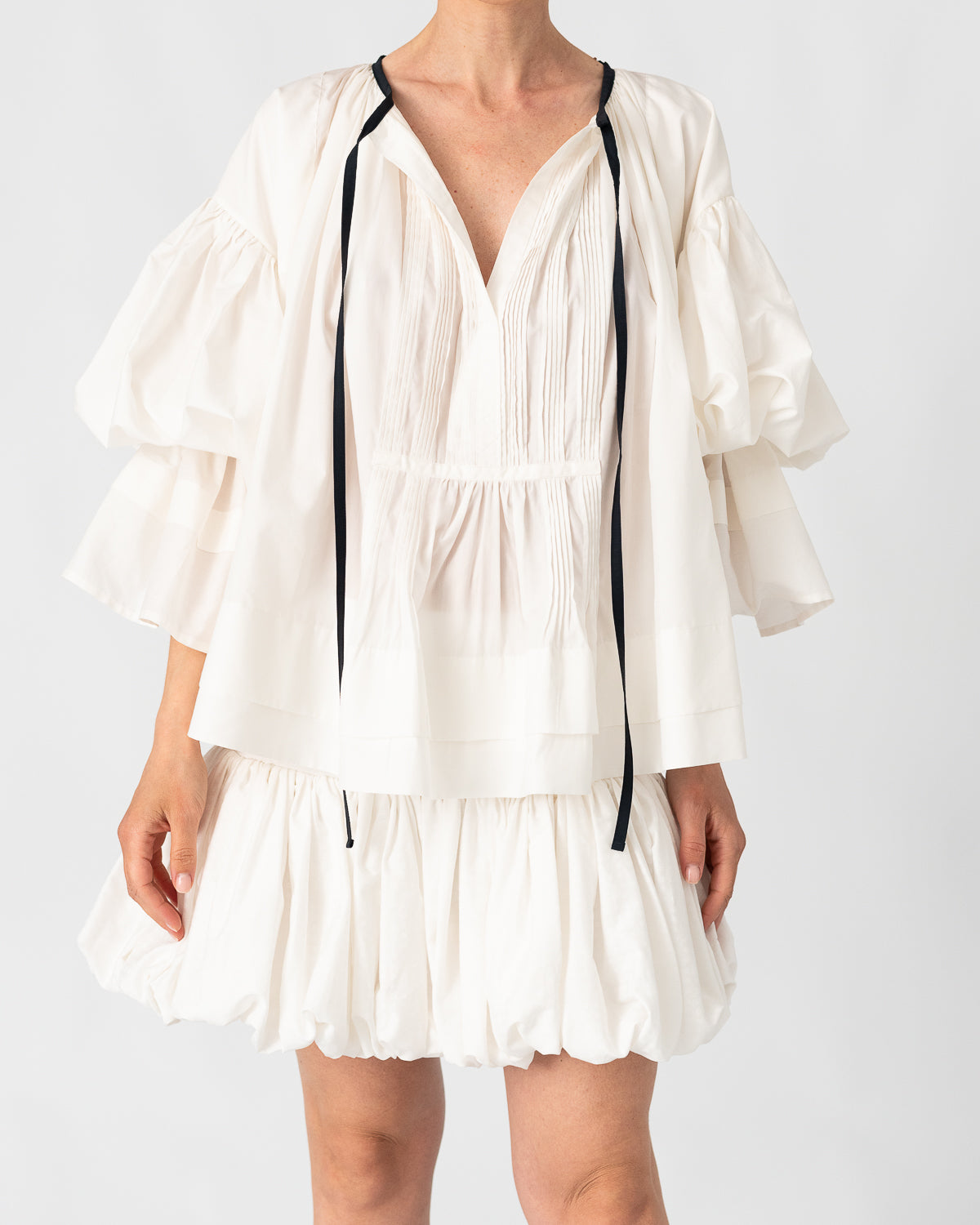 Model is wearing the Favignana Cotton and Silk Blouse by Les Vacances d’Irina, a vintage-inspired handmade blouse with pleated three-quarter sleeves, black bow neckline, and luxurious cotton-silk fabric, available at House of Woven Stories.