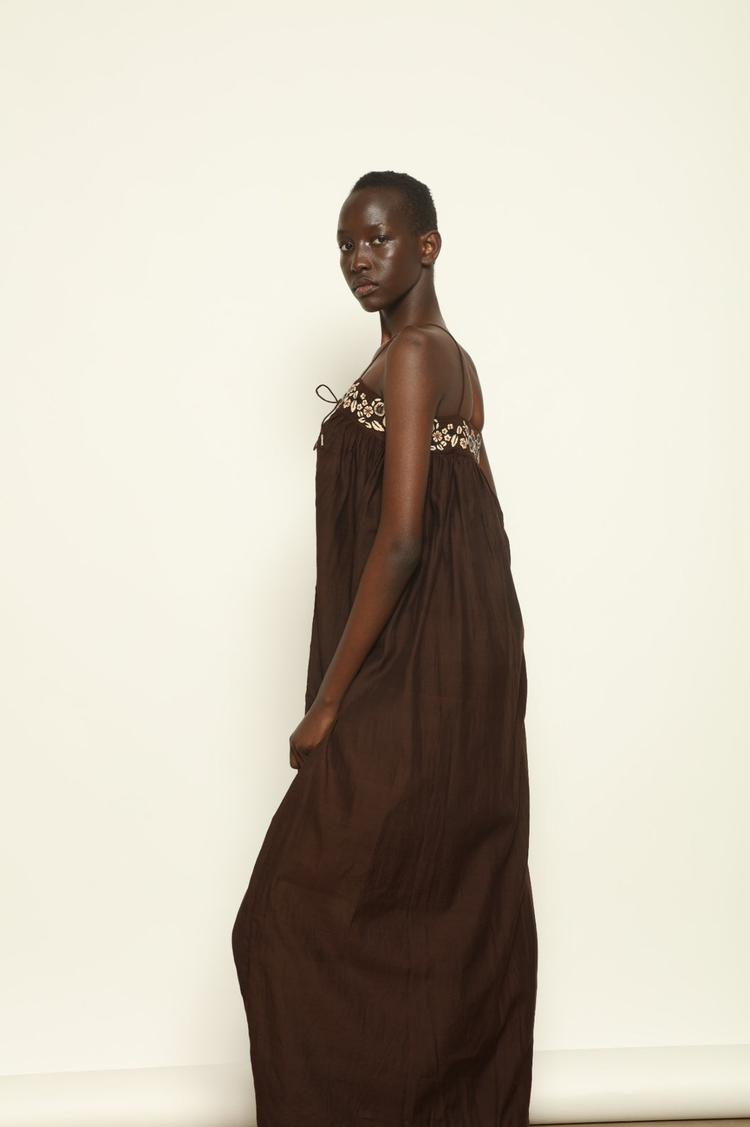 Model is wearing the Flor Brown Linen Dress by Supernaturae x HONS, crafted in heavyweight sustainable linen with a wrap-tie silhouette, earthy brown plant-dyed finish and structured yet breathable form. Made in collaboration with artisan communities in Kutch, Gujarat, this ethical resortwear piece features organic tonal variations and timeless design