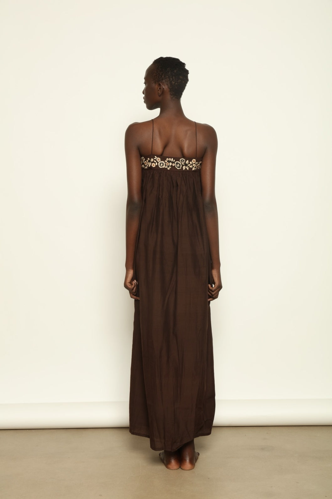 Model is wearing the Flor Brown Linen Dress by Supernaturae x HONS, crafted in heavyweight sustainable linen with a wrap-tie silhouette, earthy brown plant-dyed finish and structured yet breathable form. Made in collaboration with artisan communities in Kutch, Gujarat, this ethical resortwear piece features organic tonal variations and timeless design