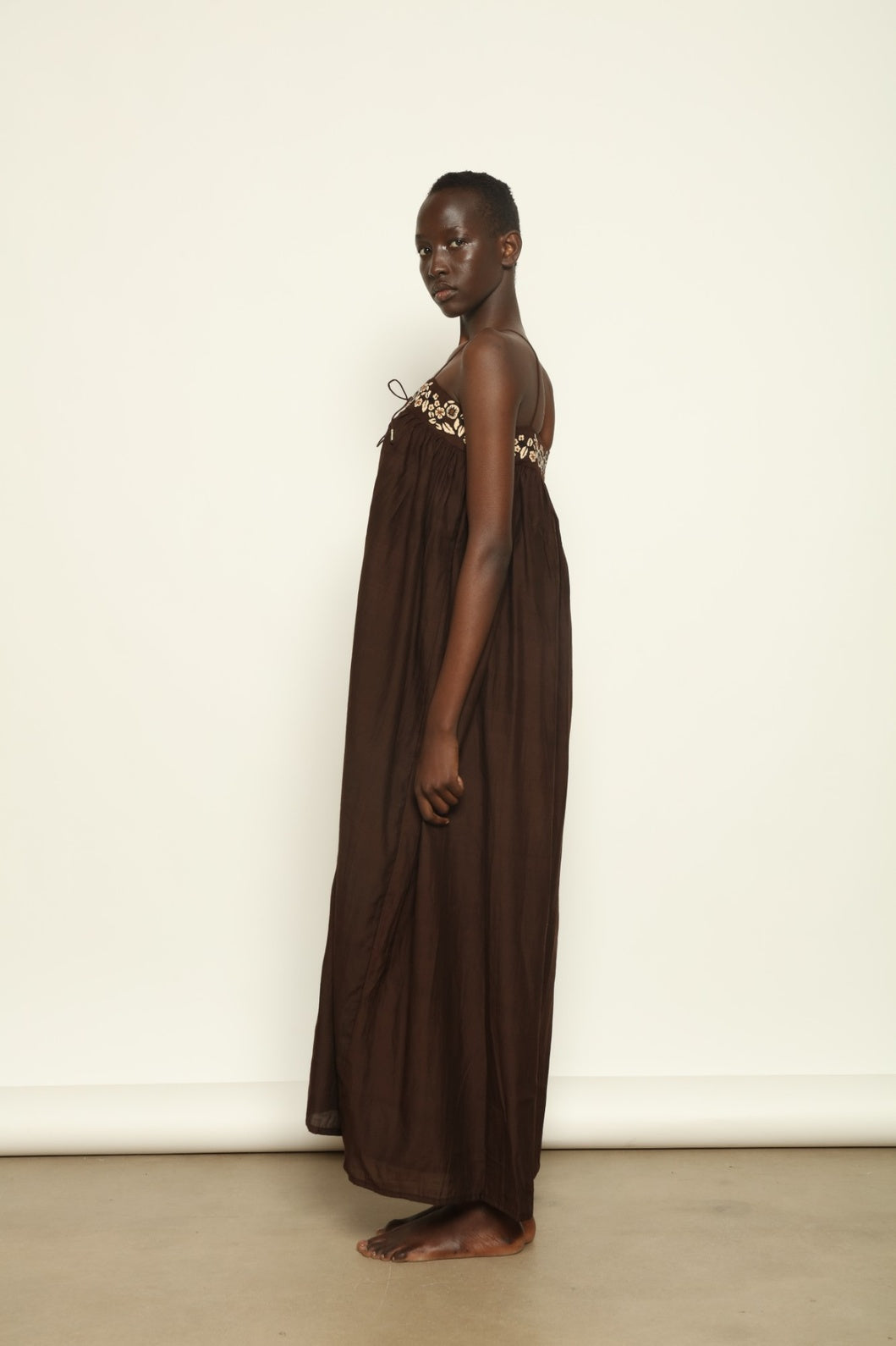 Model is wearing the Flor Brown Linen Dress by Supernaturae x HONS, crafted in heavyweight sustainable linen with a wrap-tie silhouette, earthy brown plant-dyed finish and structured yet breathable form. Made in collaboration with artisan communities in Kutch, Gujarat, this ethical resortwear piece features organic tonal variations and timeless design