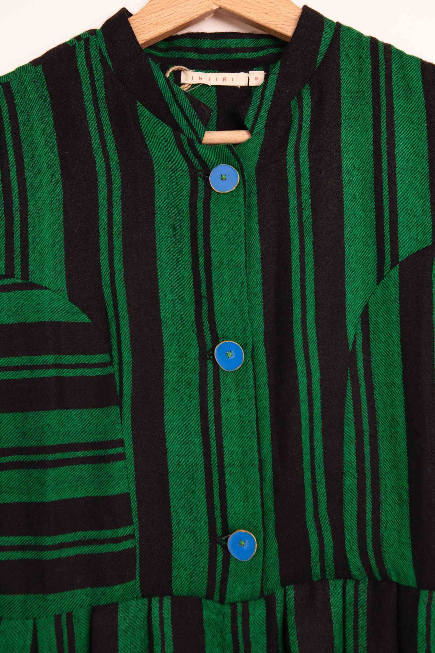 Model is wearing the Folklore 34 silk and wool striped dress by Injiri, featuring bold green and black stripes and sky blue buttons, artisan-made in India.