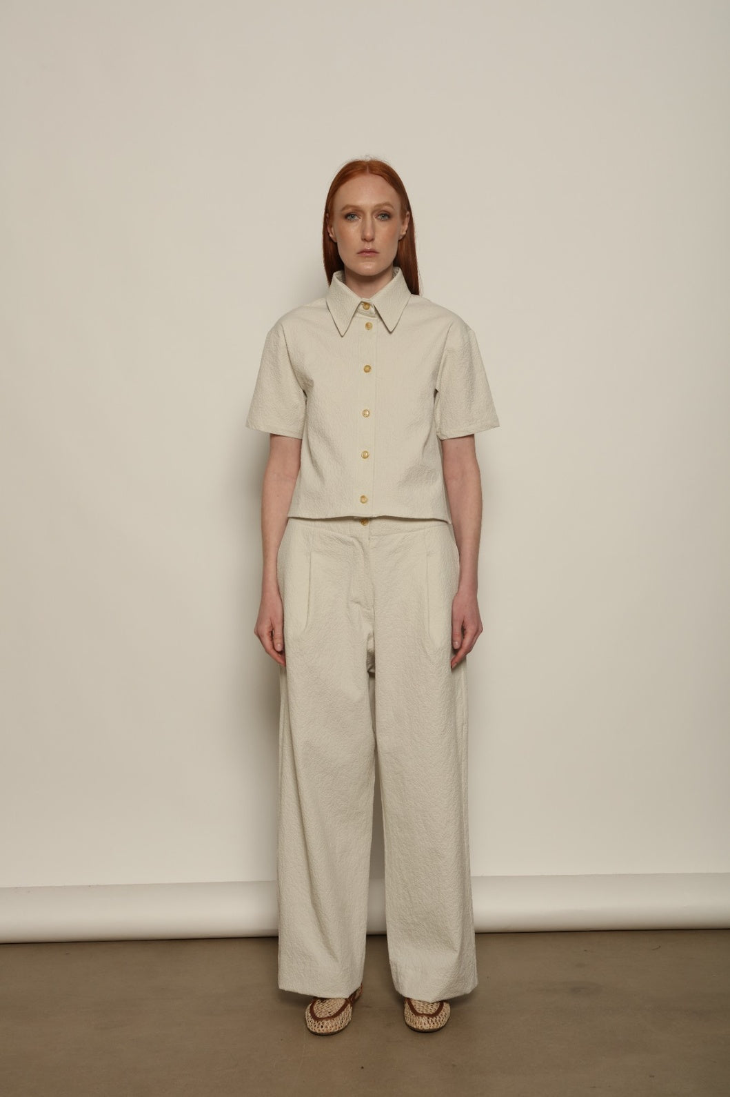 Model is wearing the Gabriella seersucker trousers from the House of Woven Stories selection, lightweight and breathable women’s summer pants made in Italy, featuring a relaxed tailored silhouette designed for effortless movement and warm weather.