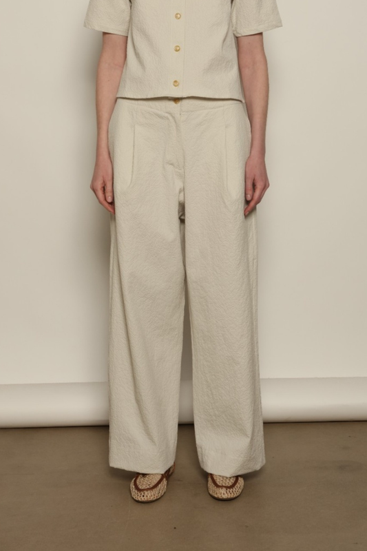 Model is wearing the Gabriella seersucker trousers from the House of Woven Stories selection, lightweight and breathable women’s summer pants made in Italy, featuring a relaxed tailored silhouette designed for effortless movement and warm weather.