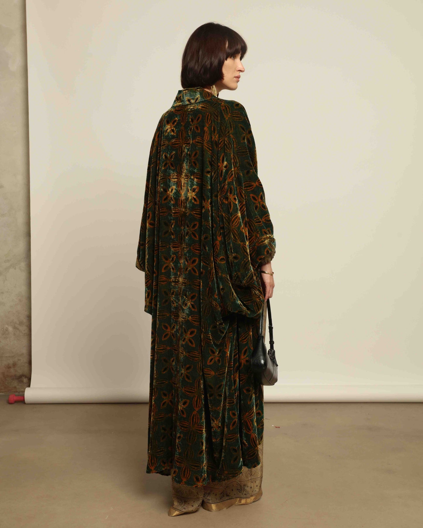 Model is wearing a golden sage silk and velvet abaya with geometric patterns, featuring a flowing elegant silhouette, perfect for modern and regal styling.