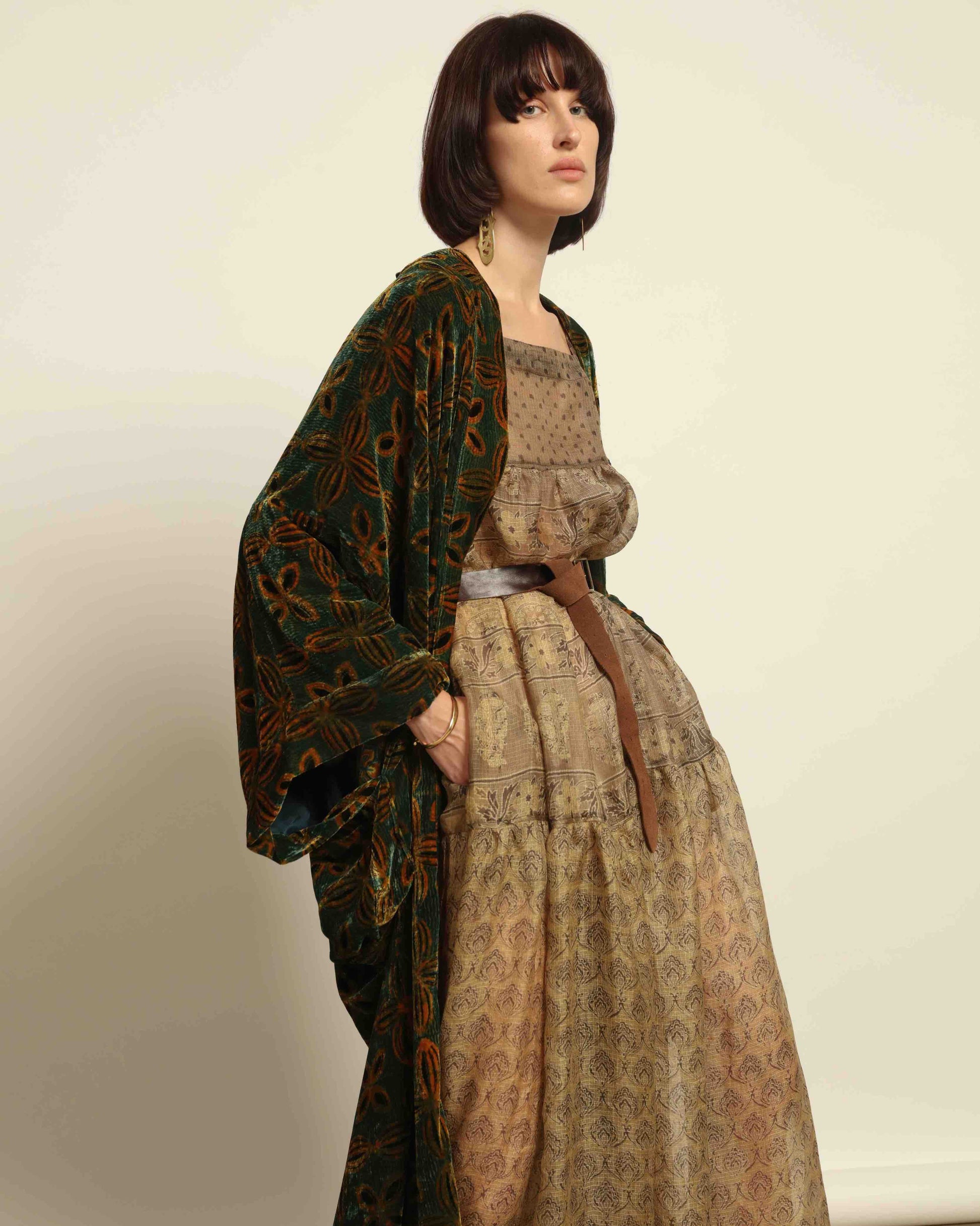 Model is wearing a golden sage silk and velvet abaya with geometric patterns, featuring a flowing elegant silhouette, perfect for modern and regal styling.