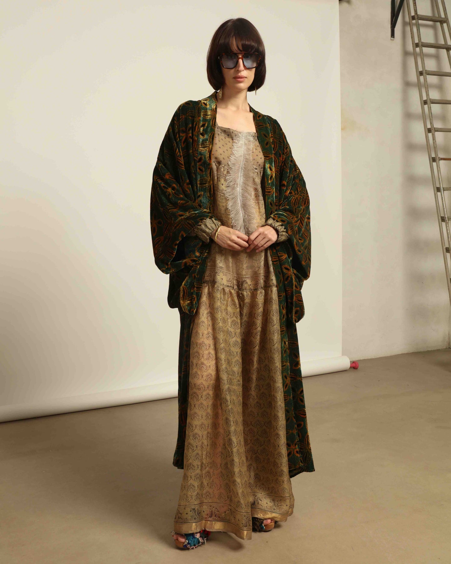 Model is wearing a golden sage silk and velvet abaya with geometric patterns, featuring a flowing elegant silhouette, perfect for modern and regal styling.