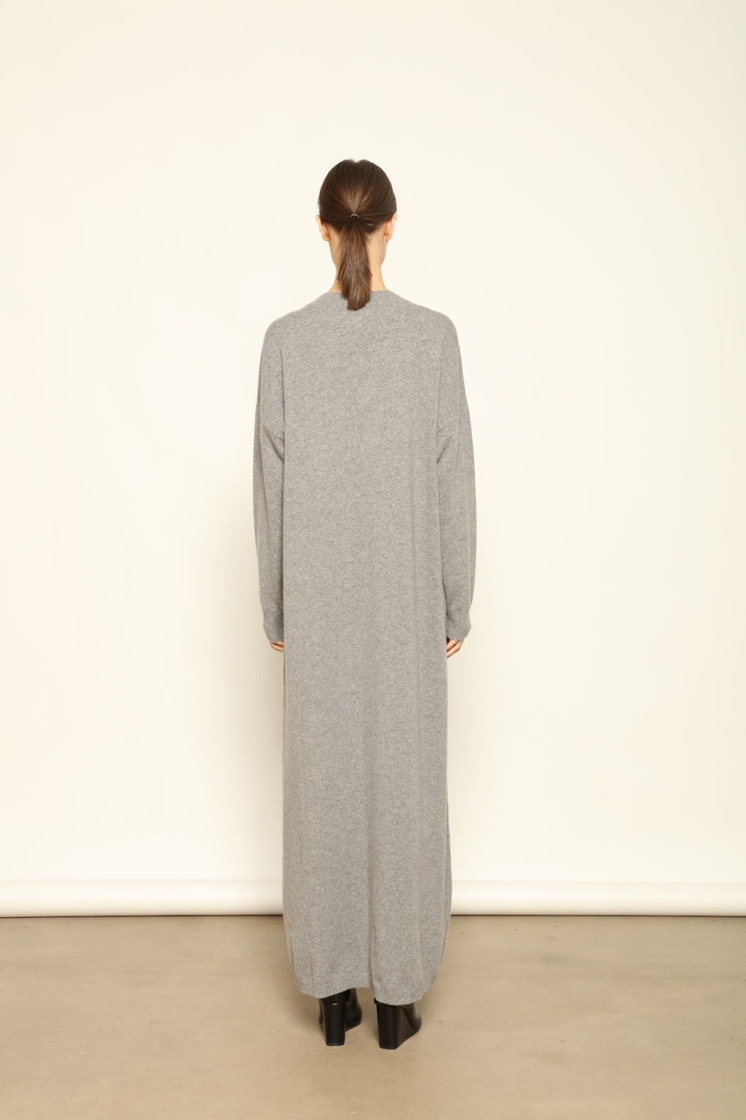 Model is wearing the Graphite Katharina V-Neck Cashmere Maxi Dress by House of Woven Stories, made from 100% pure Inner Mongolia cashmere, featuring a soft, breathable, warm knit with a long flowing silhouette, deep V-neckline, and timeless ethical luxury craftsmanship