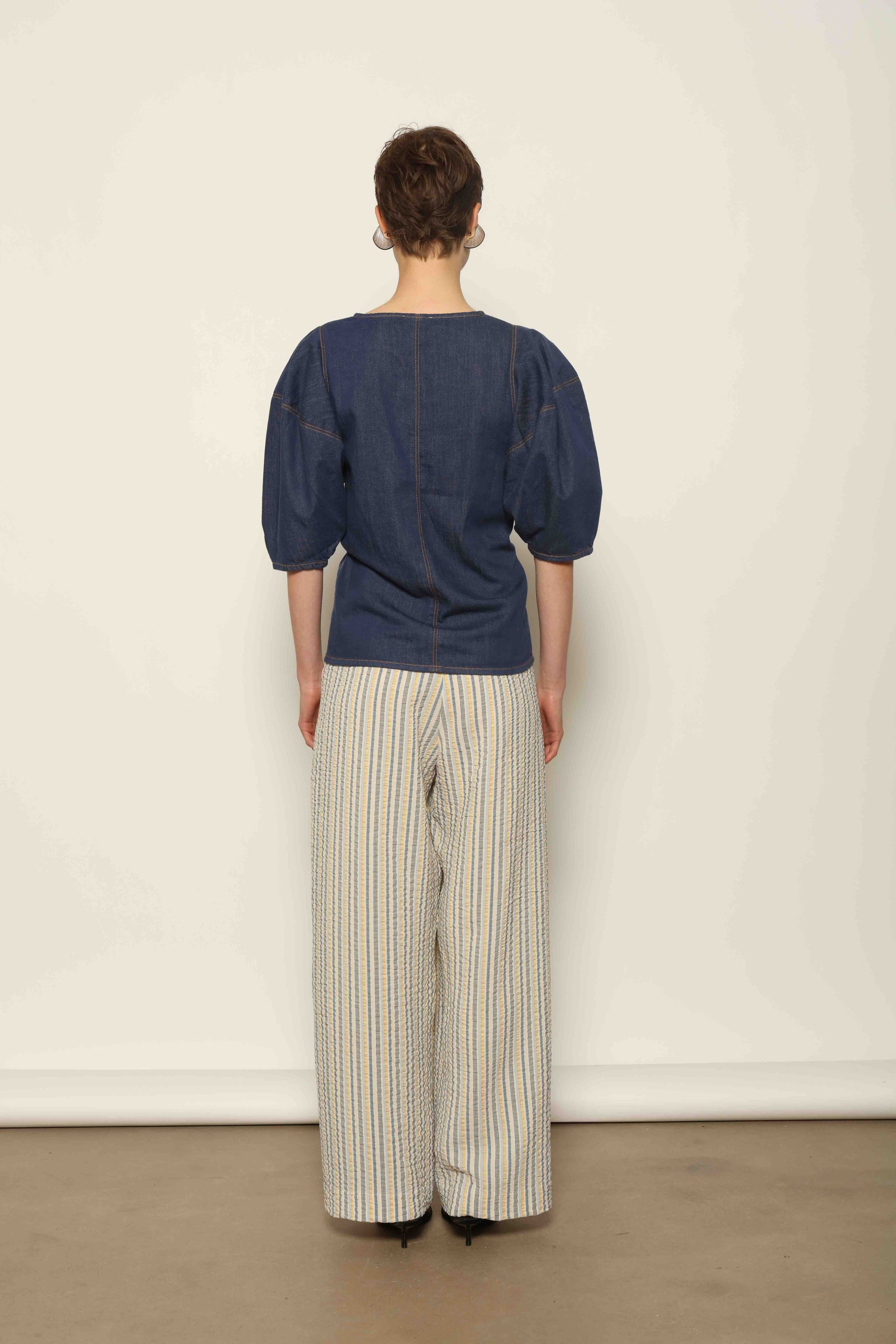 Model wearing the Blouse Bubble Brut in cotton denim by Happy Haus, featuring balloon sleeves, straight-cut silhouette, round neckline, and tobacco topstitching in a lightweight, breathable fabric.