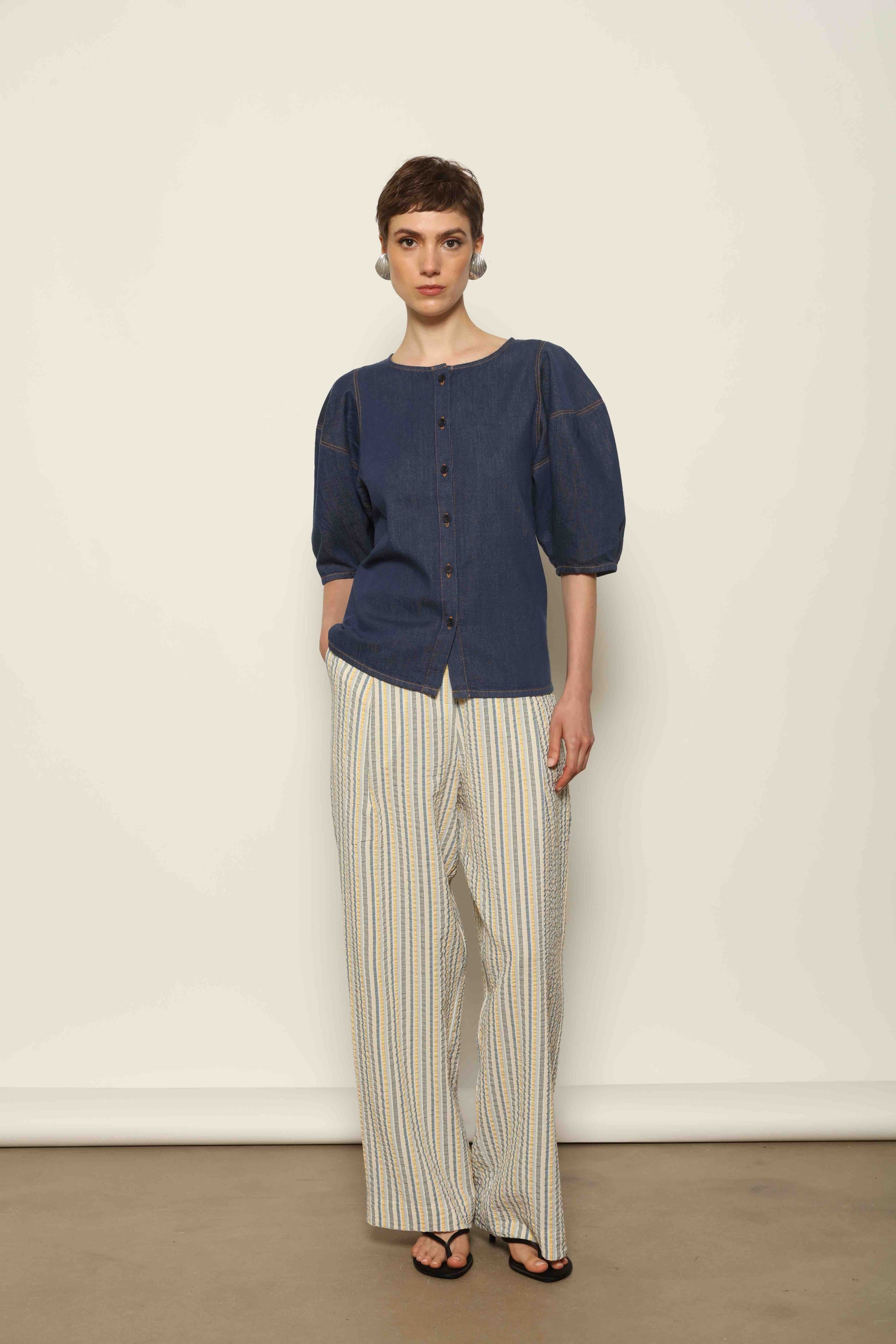 Model wearing the Blouse Bubble Brut in cotton denim by Happy Haus, featuring balloon sleeves, straight-cut silhouette, round neckline, and tobacco topstitching in a lightweight, breathable fabric.