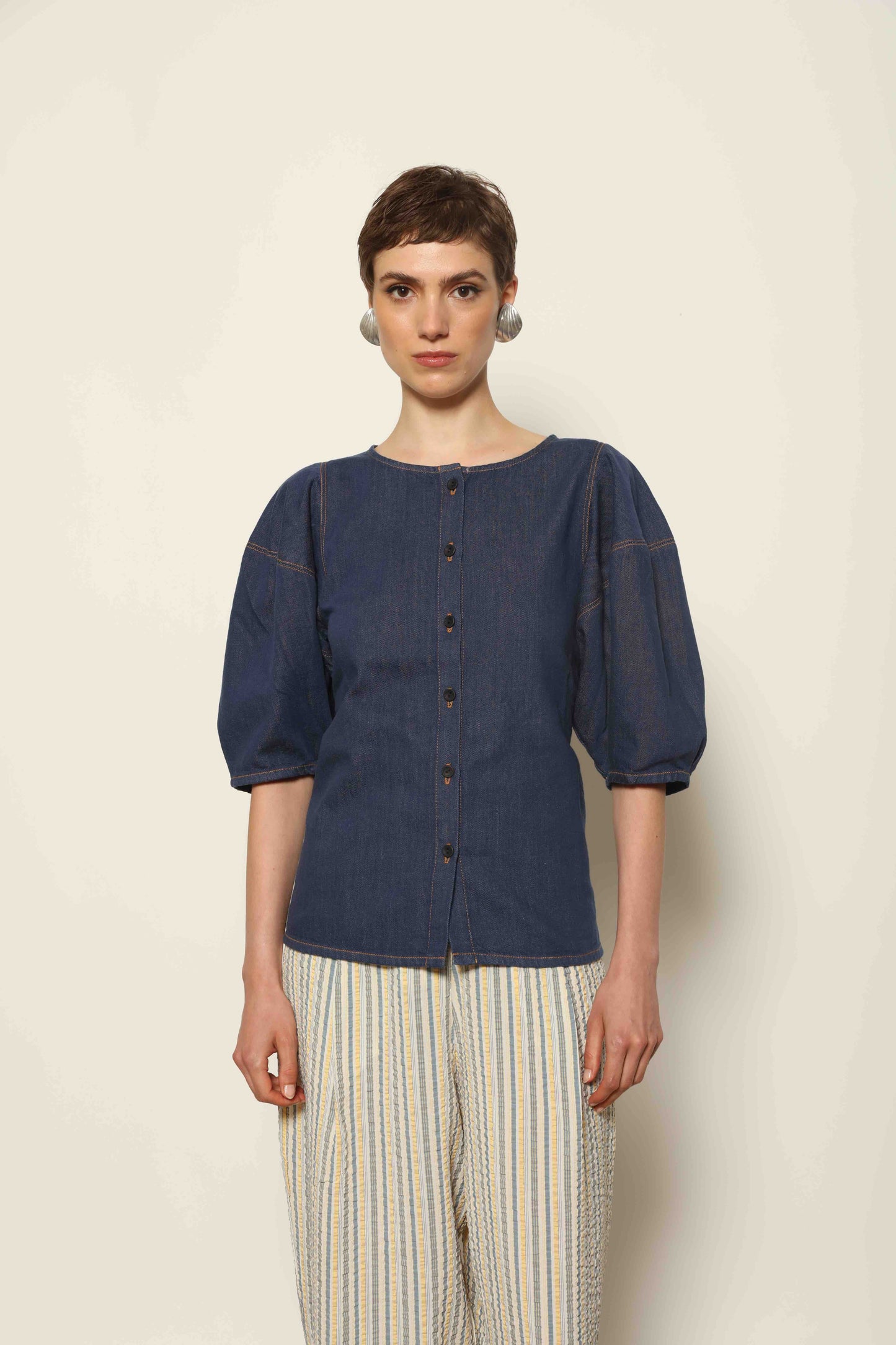 Model wearing the Blouse Bubble Brut in cotton denim by Happy Haus, featuring balloon sleeves, straight-cut silhouette, round neckline, and tobacco topstitching in a lightweight, breathable fabric.