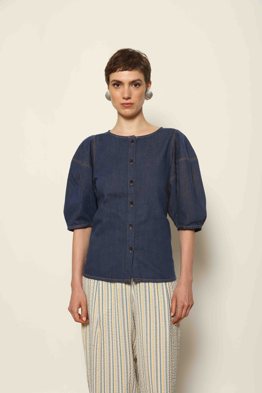 Model wearing the Blouse Bubble Brut in cotton denim by Happy Haus, featuring balloon sleeves, straight-cut silhouette, round neckline, and tobacco topstitching in a lightweight, breathable fabric.