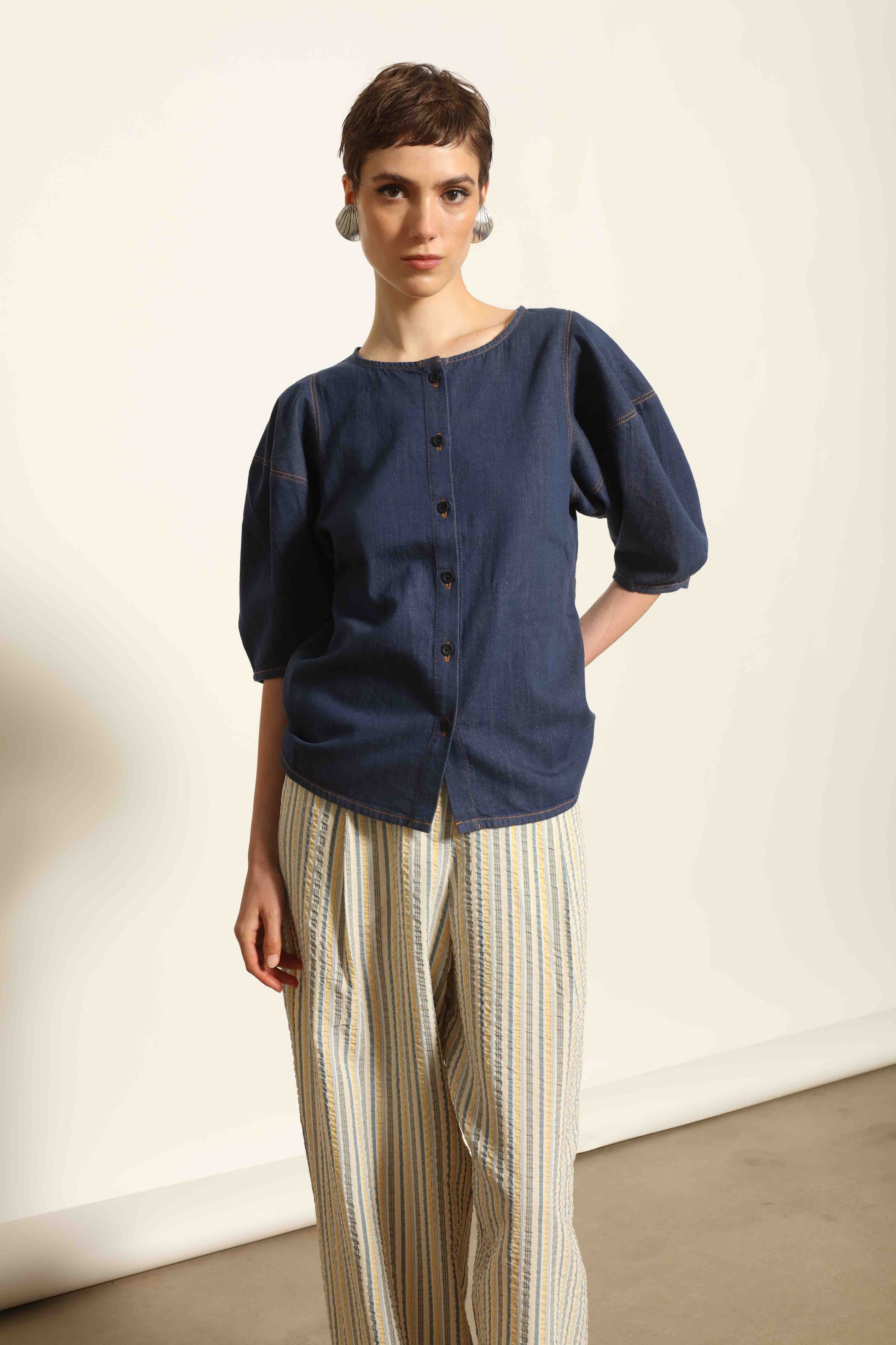 Model wearing the Blouse Bubble Brut in cotton denim by Happy Haus, featuring balloon sleeves, straight-cut silhouette, round neckline, and tobacco topstitching in a lightweight, breathable fabric.