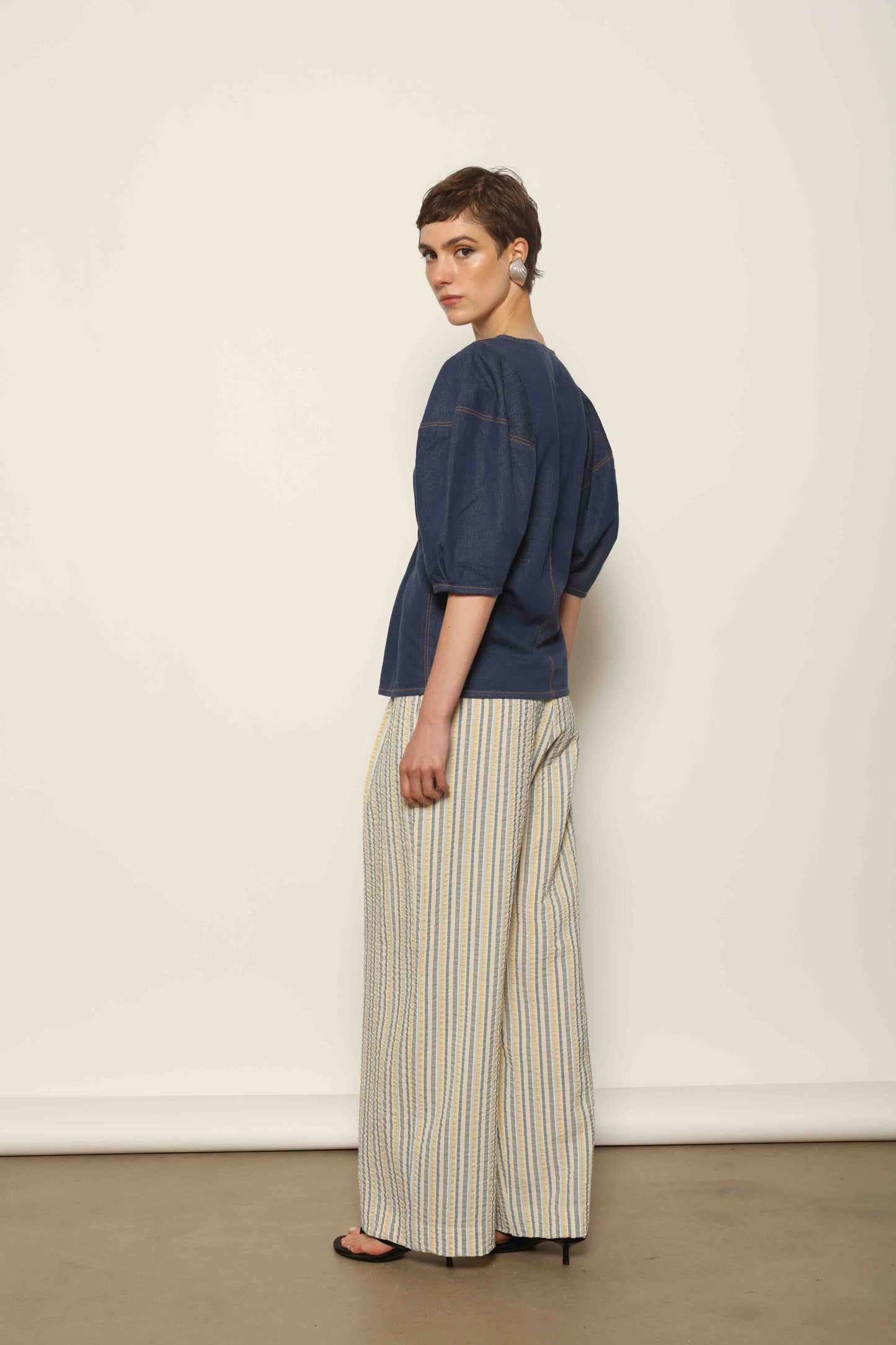 Model wearing the Blouse Bubble Brut in cotton denim by Happy Haus, featuring balloon sleeves, straight-cut silhouette, round neckline, and tobacco topstitching in a lightweight, breathable fabric.