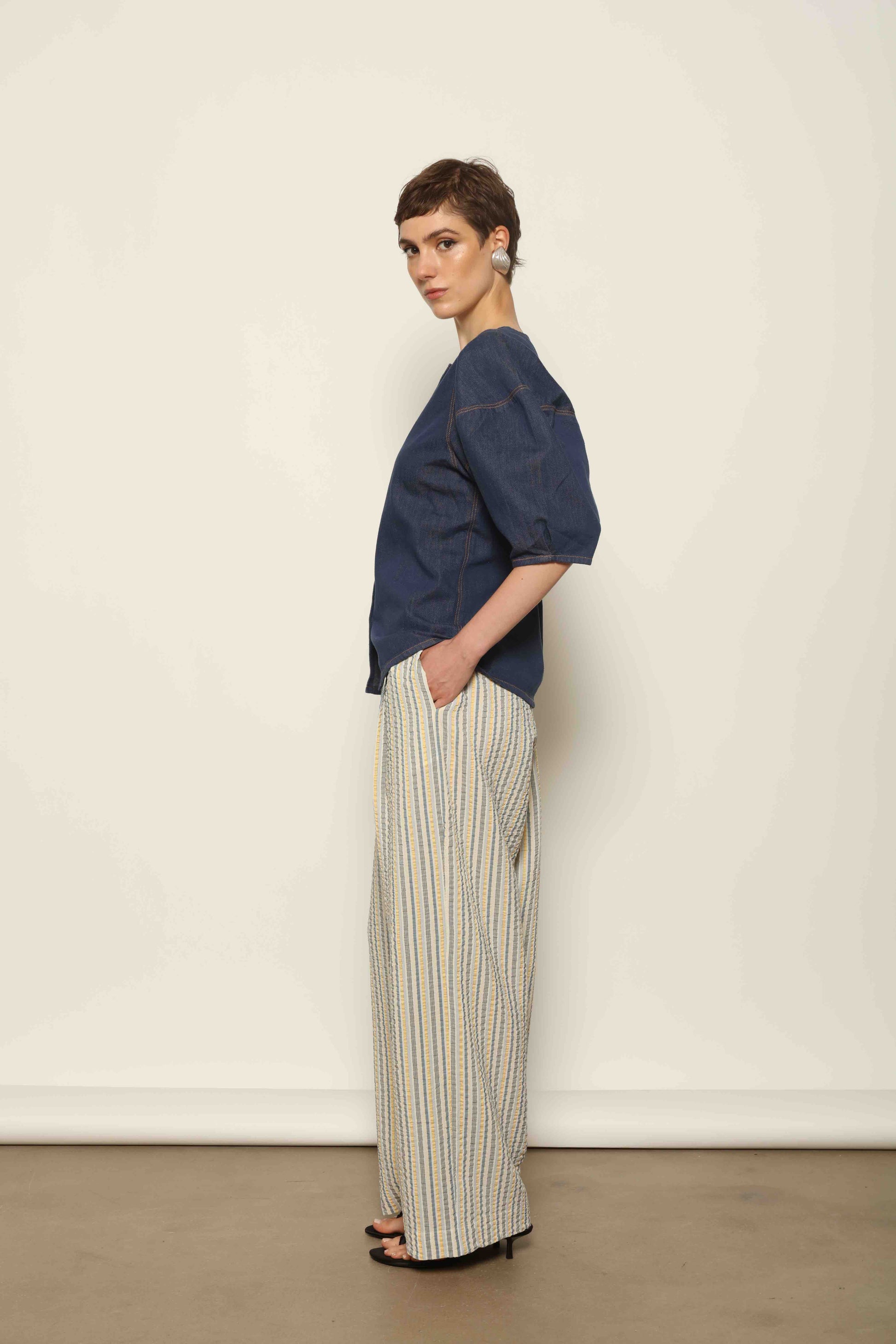 Model wearing the Blouse Bubble Brut in cotton denim by Happy Haus, featuring balloon sleeves, straight-cut silhouette, round neckline, and tobacco topstitching in a lightweight, breathable fabric.