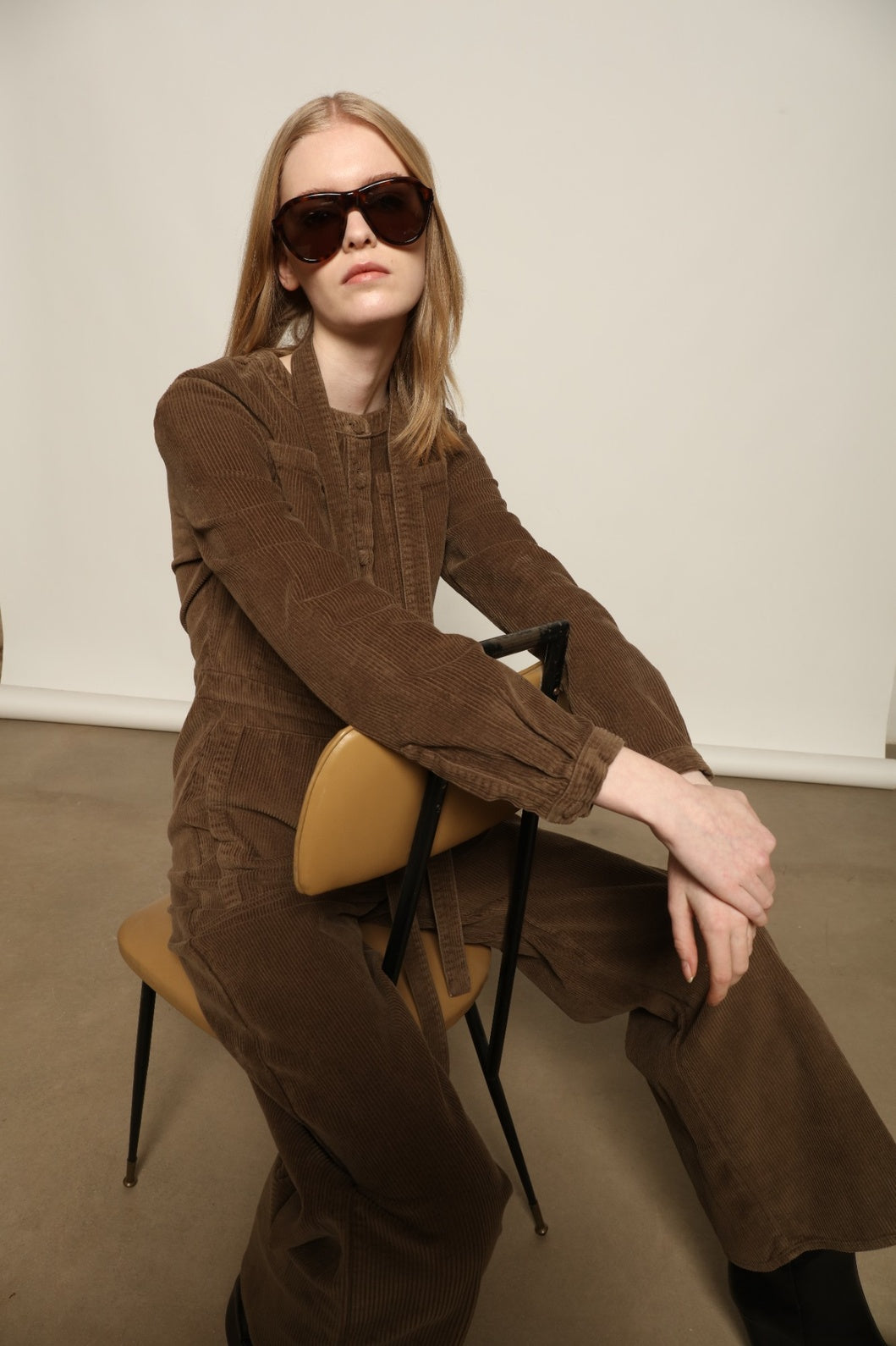 Model is wearing La Combinaison 4 Poches by Happy Haus, a bronze cotton velour jumpsuit with corozo buttons, chest and hip patch pockets, removable belt and relaxed cuffs, curated in the House of Woven Stories selection