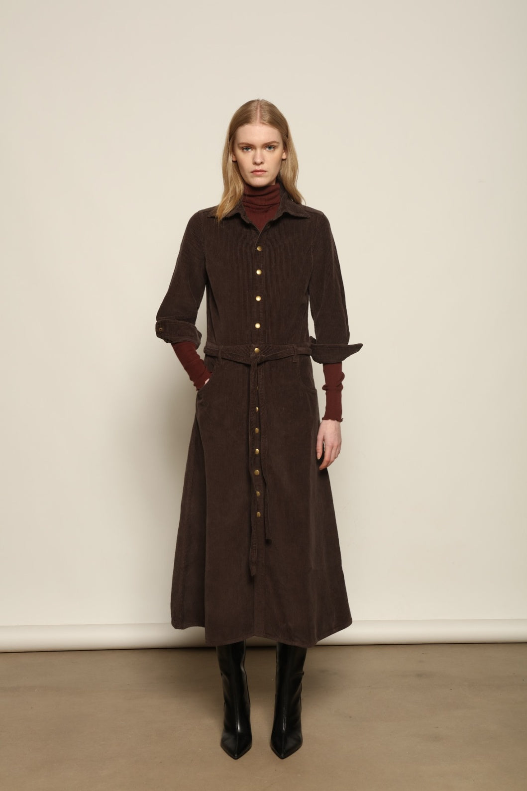 Model is wearing La Robe Trompe L’Oeil in Chocolate by Happy Haus, a corduroy cotton trompe-l’œil dress with removable belt, tulip-shaped pockets and brass snaps, curated in the House of Woven Stories selection.