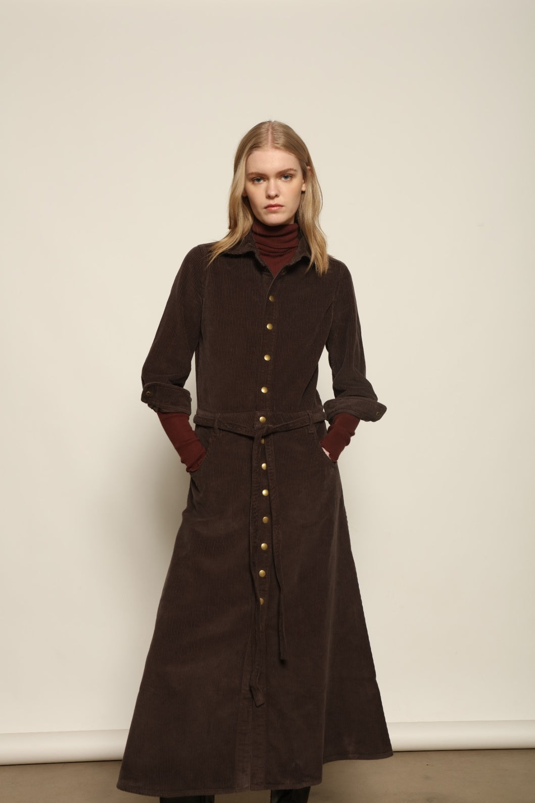 Model is wearing La Robe Trompe L’Oeil in Chocolate by Happy Haus, a corduroy cotton trompe-l’œil dress with removable belt, tulip-shaped pockets and brass snaps, curated in the House of Woven Stories selection.