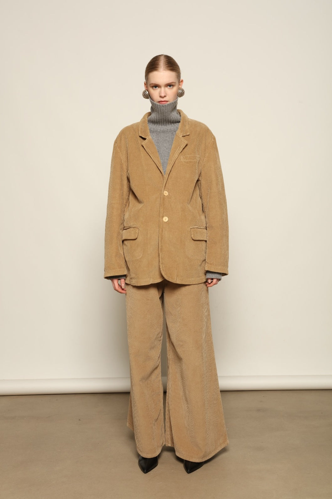 Model is wearing Le Blazer in Vintage Beige by Happy Haus, a GOTS-certified Italian corduroy cotton tailored jacket with relaxed straight silhouette, flap pockets, wooden buttons and soft back slit, curated in the House of Woven Stories selection.