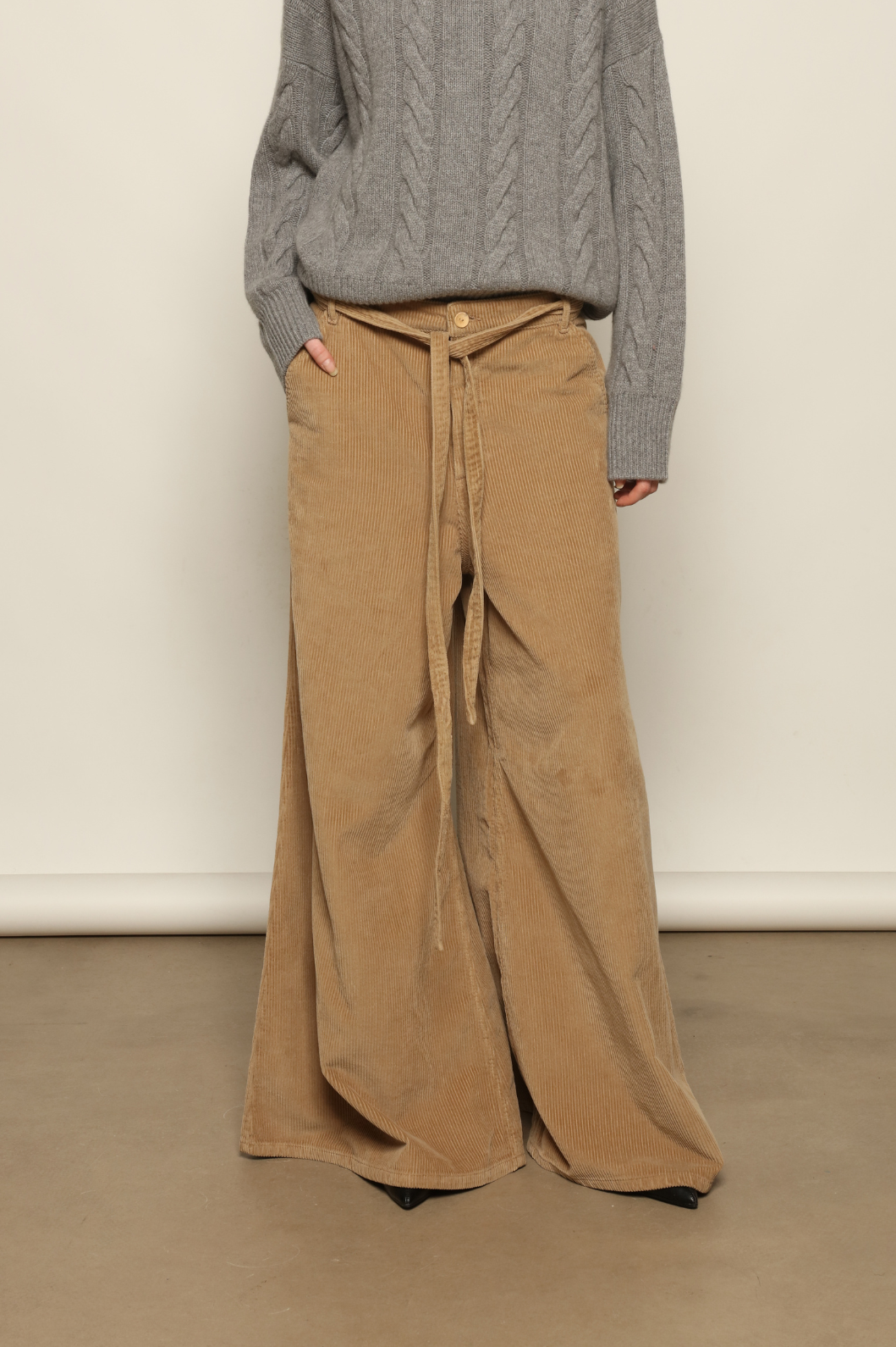 Model is wearing Le Pantalon Over Chino in Beige by Happy Haus, flared oversized corduroy cotton trousers with removable belt, corozo buttons and peacock embroidery, curated in the House of Woven Stories selection.