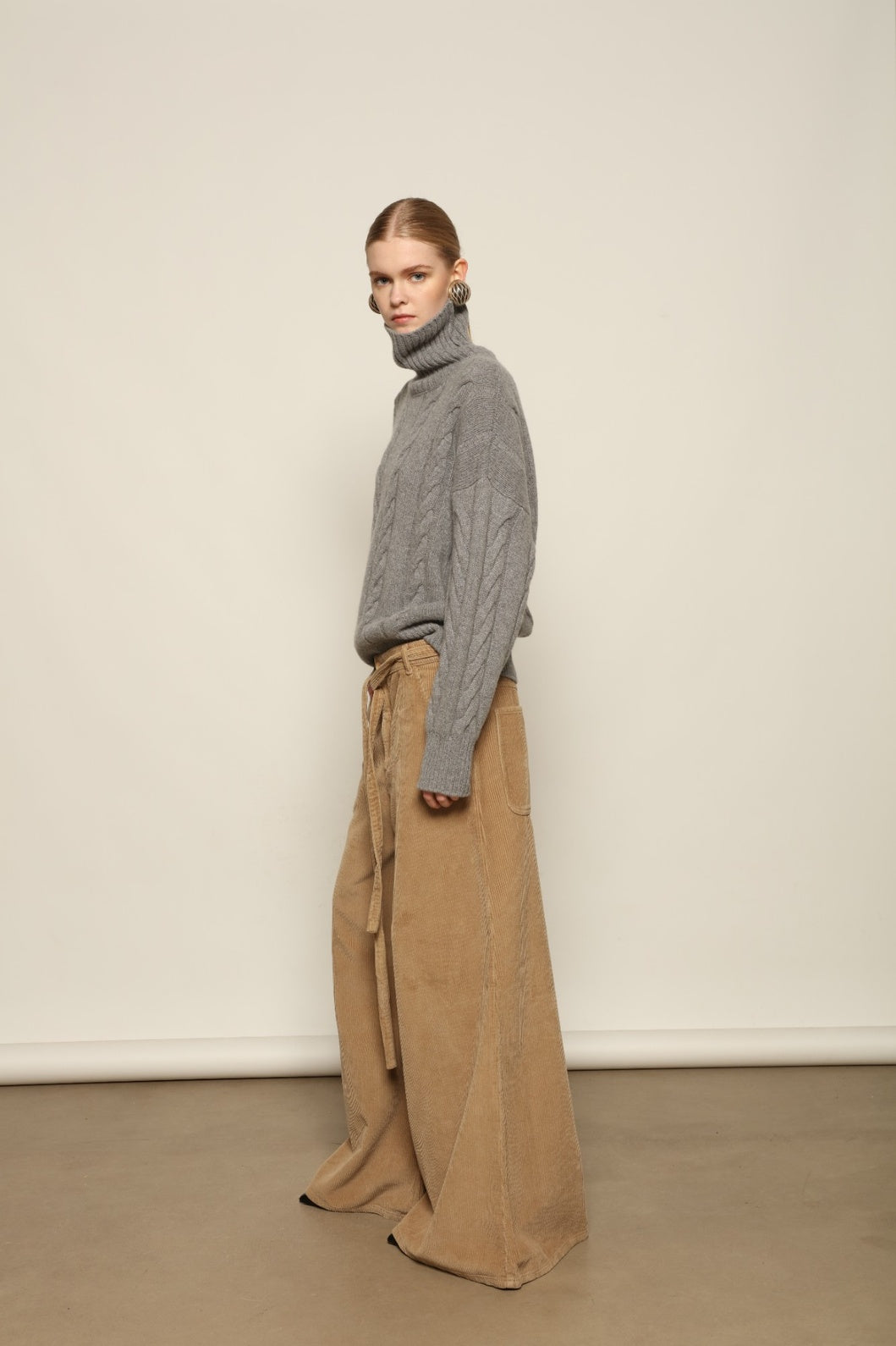 Model is wearing Le Pantalon Over Chino in Beige by Happy Haus, flared oversized corduroy cotton trousers with removable belt, corozo buttons and peacock embroidery, curated in the House of Woven Stories selection.