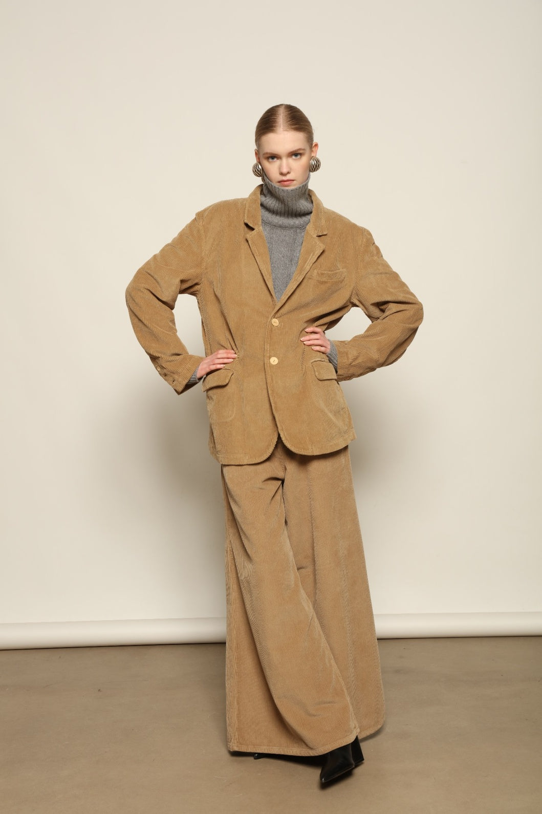 Model is wearing Le Pantalon Over Chino in Beige by Happy Haus, flared oversized corduroy cotton trousers with removable belt, corozo buttons and peacock embroidery, curated in the House of Woven Stories selection.