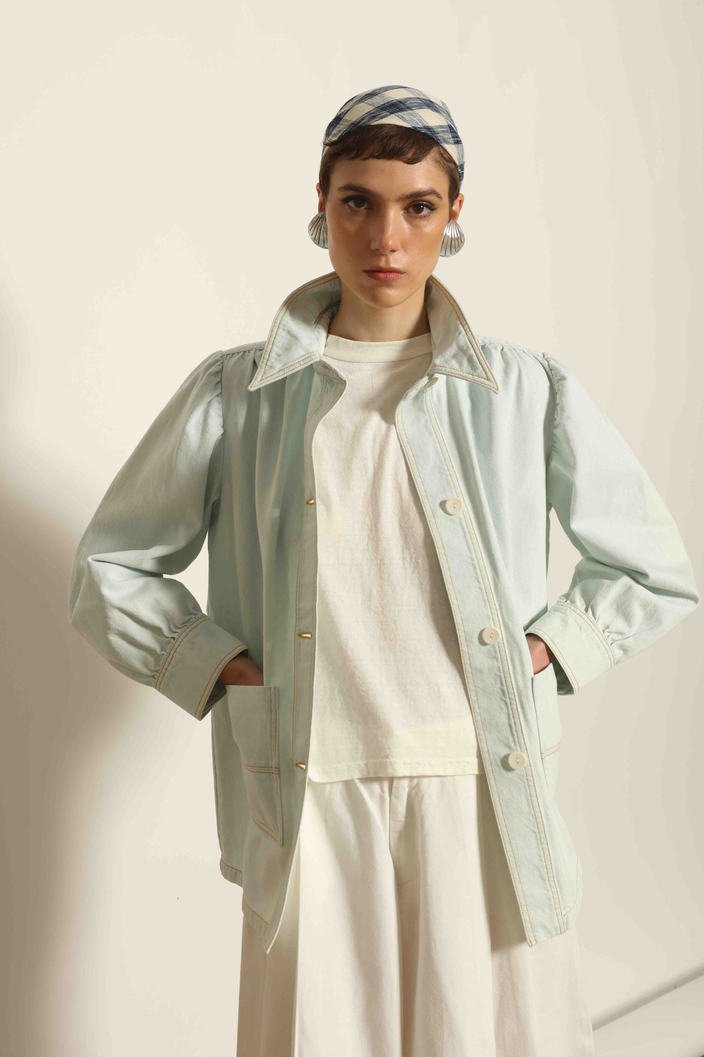 Model wearing the La Veste Peintre in Summer Blue by Happy Haus from the House of Nomad Stories collection, featuring a relaxed fit, light blue denim, patch pockets, wooden button closure, and workwear-inspired design.