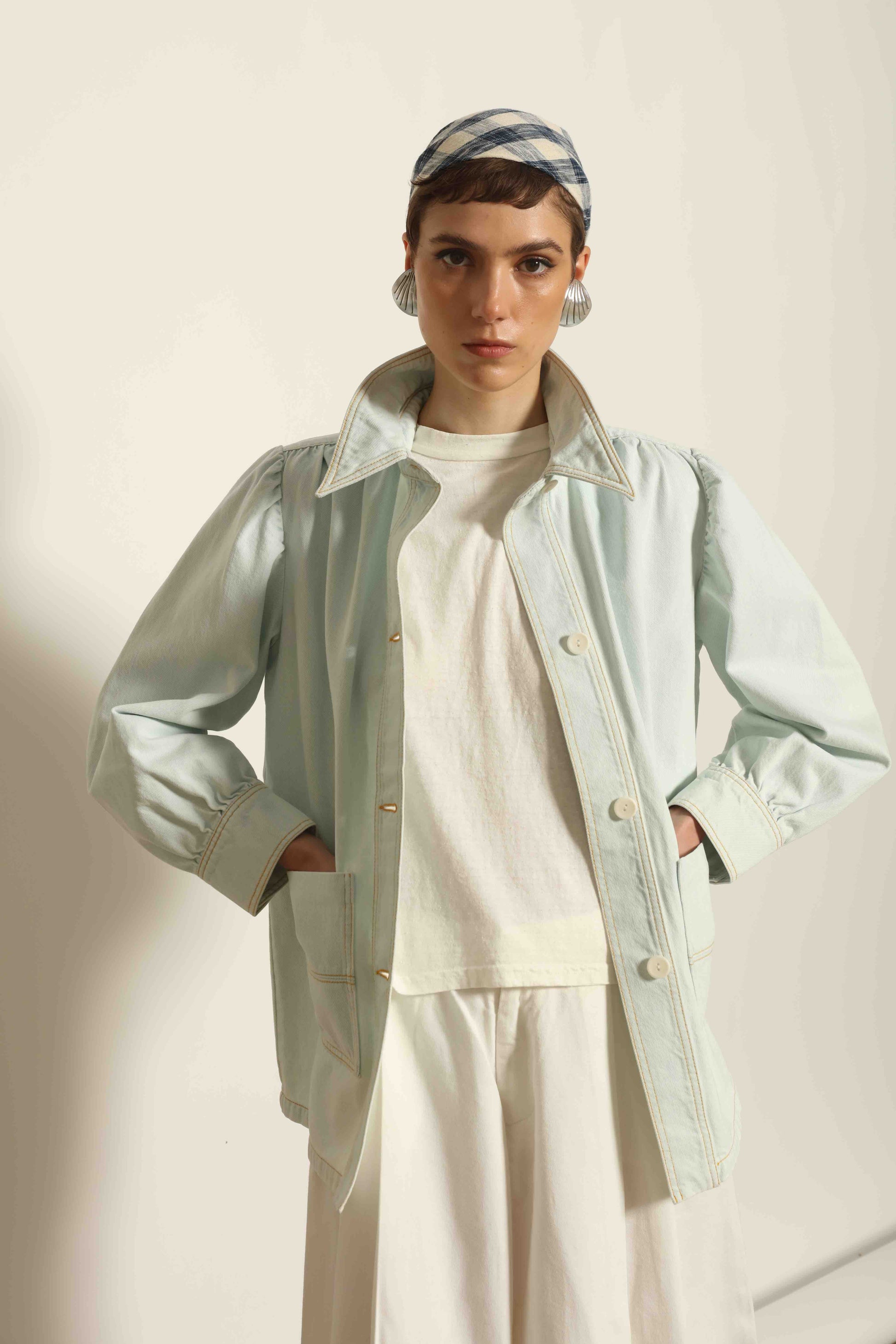 Model wearing the La Veste Peintre in Summer Blue by Happy Haus from the House of Nomad Stories collection, featuring a relaxed fit, light blue denim, patch pockets, wooden button closure, and workwear-inspired design.