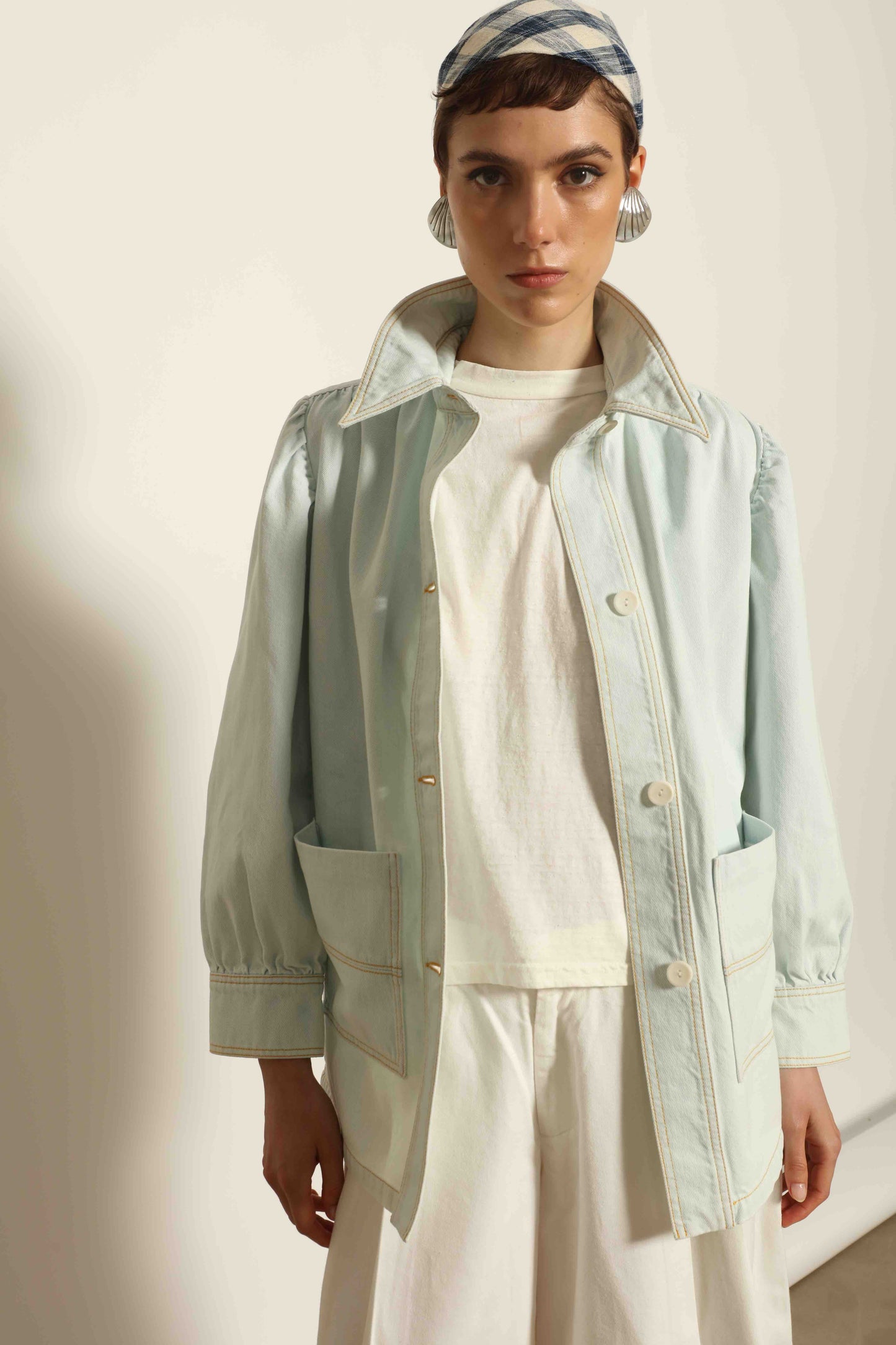 Model wearing the La Veste Peintre in Summer Blue by Happy Haus from the House of Nomad Stories collection, featuring a relaxed fit, light blue denim, patch pockets, wooden button closure, and workwear-inspired design.