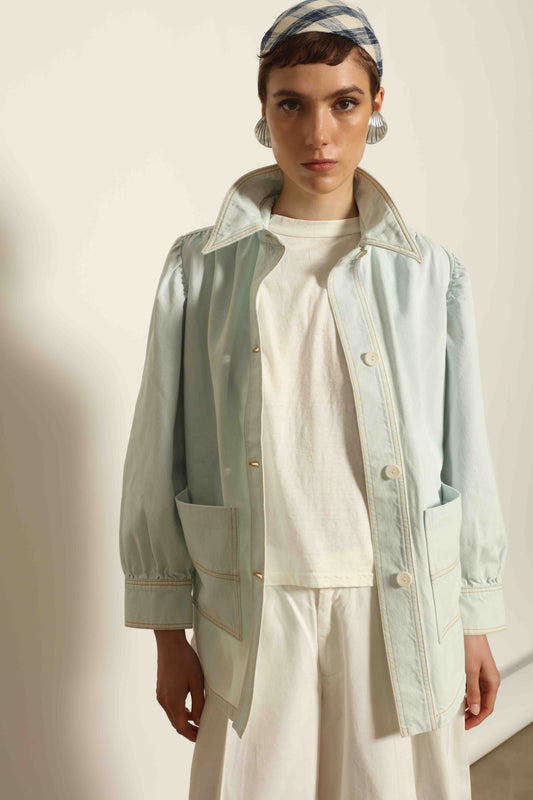 Model wearing the La Veste Peintre in Summer Blue by Happy Haus from the House of Nomad Stories collection, featuring a relaxed fit, light blue denim, patch pockets, wooden button closure, and workwear-inspired design.