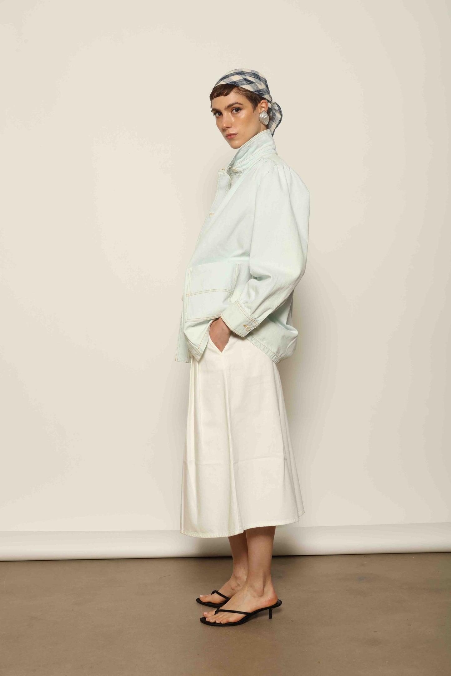 Model wearing the La Veste Peintre in Summer Blue by Happy Haus from the House of Nomad Stories collection, featuring a relaxed fit, light blue denim, patch pockets, wooden button closure, and workwear-inspired design.