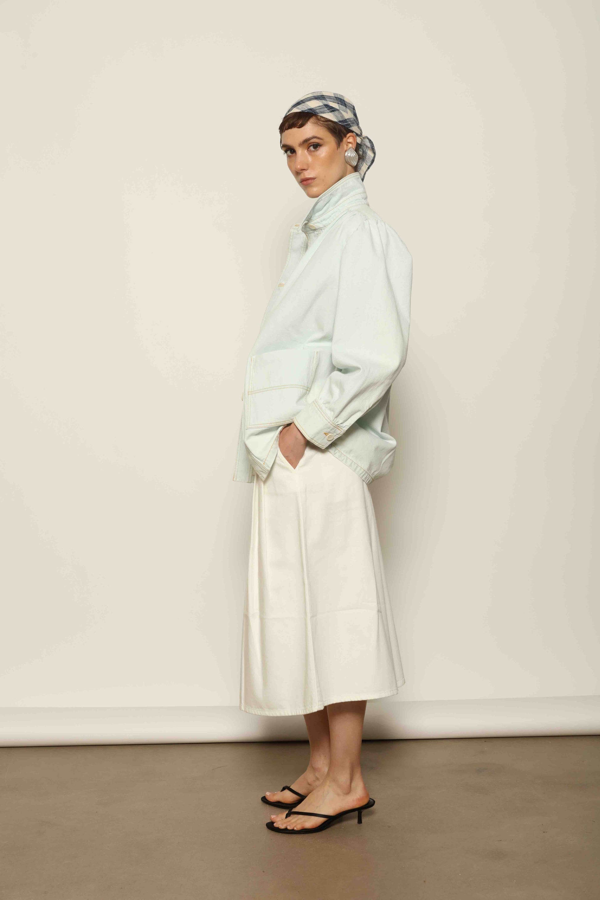 Model wearing the La Veste Peintre in Summer Blue by Happy Haus from the House of Nomad Stories collection, featuring a relaxed fit, light blue denim, patch pockets, wooden button closure, and workwear-inspired design.