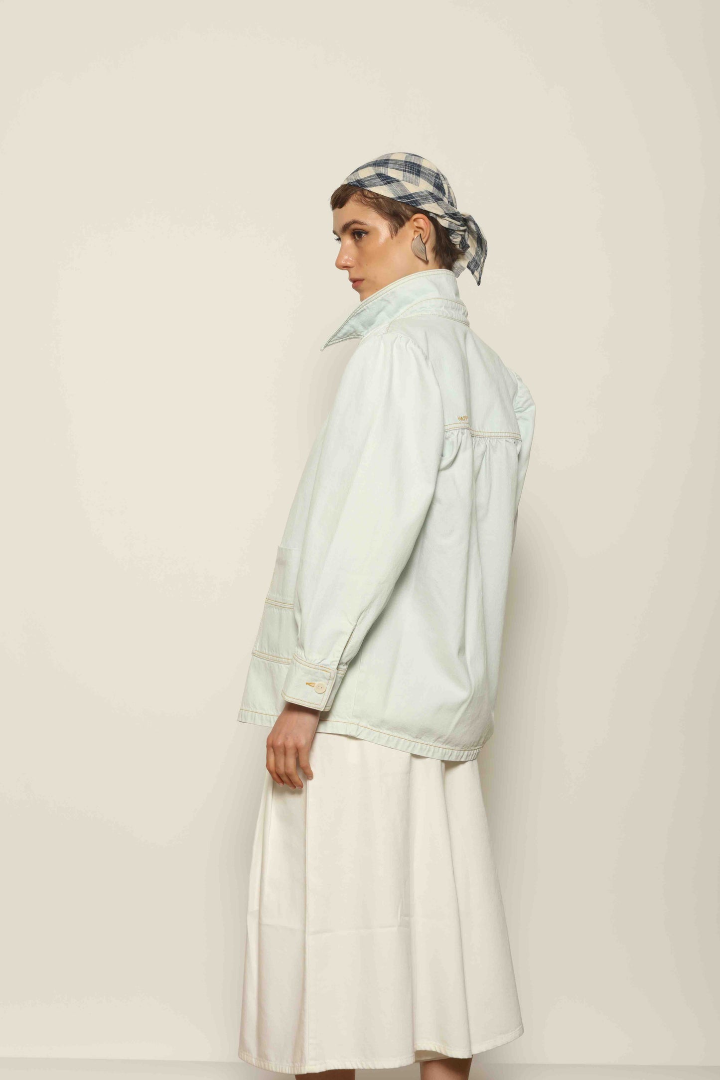 Model wearing the La Veste Peintre in Summer Blue by Happy Haus from the House of Nomad Stories collection, featuring a relaxed fit, light blue denim, patch pockets, wooden button closure, and workwear-inspired design.
