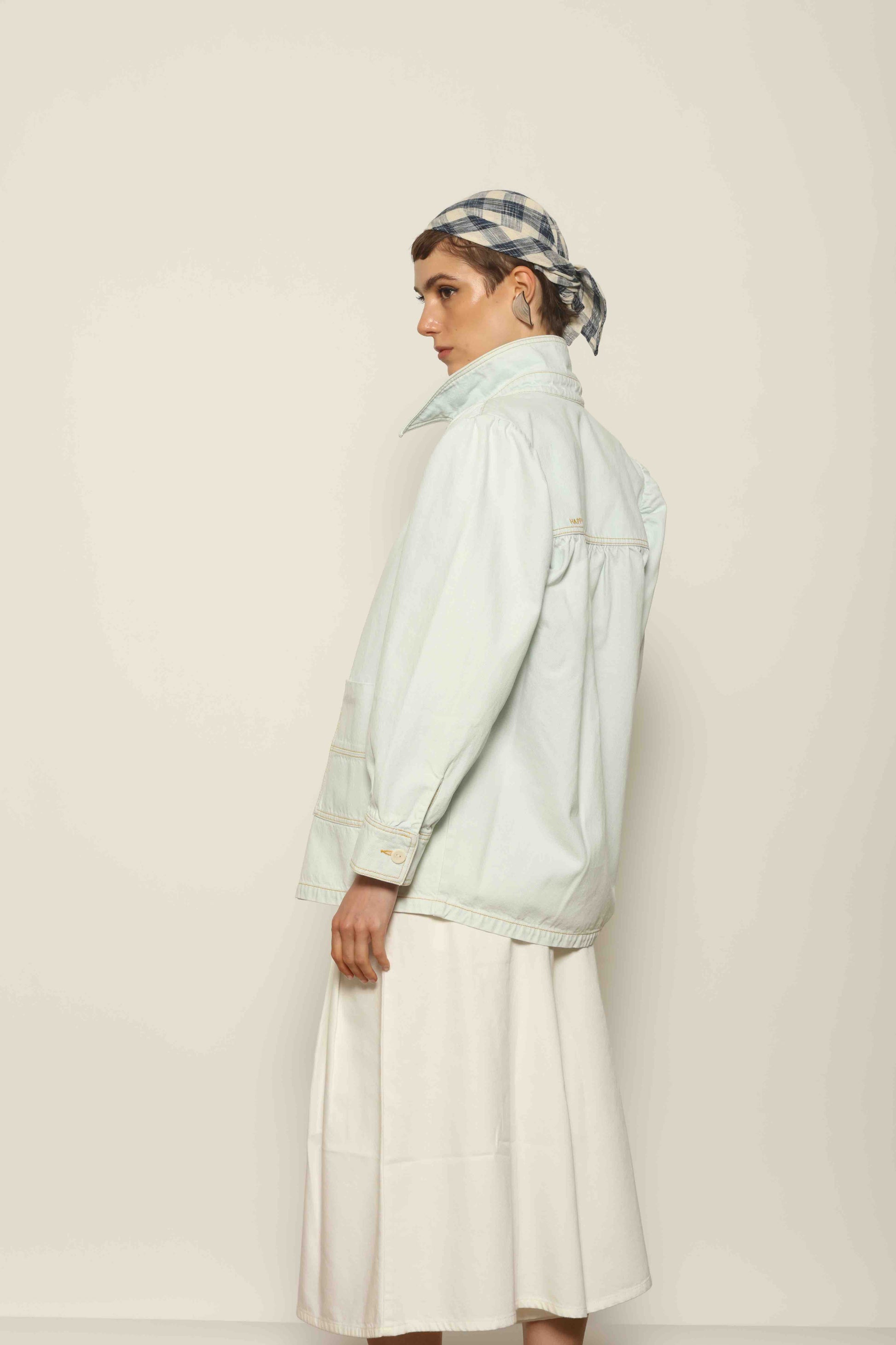 Model wearing the La Veste Peintre in Summer Blue by Happy Haus from the House of Nomad Stories collection, featuring a relaxed fit, light blue denim, patch pockets, wooden button closure, and workwear-inspired design.