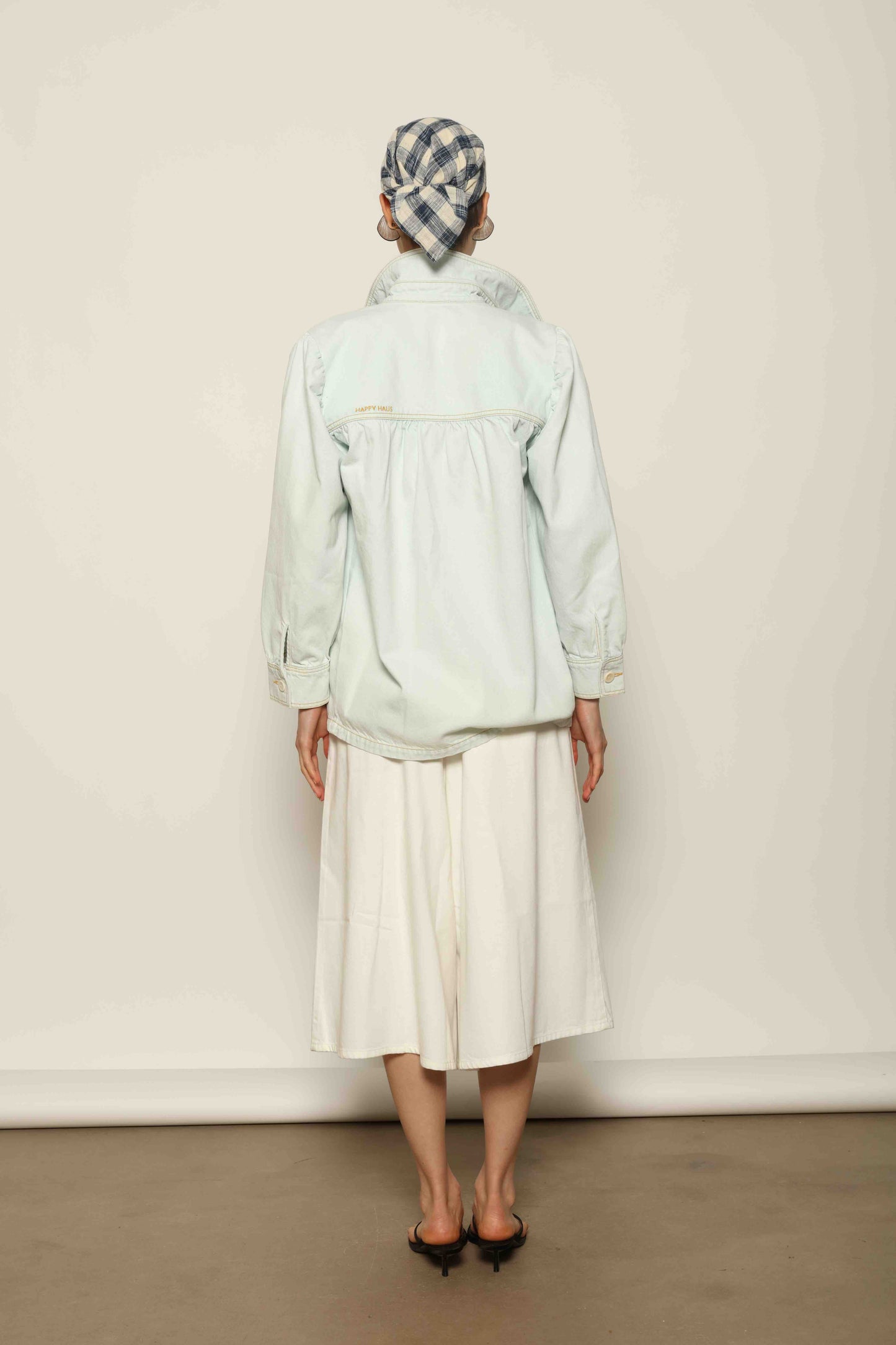Model wearing the La Veste Peintre in Summer Blue by Happy Haus from the House of Nomad Stories collection, featuring a relaxed fit, light blue denim, patch pockets, wooden button closure, and workwear-inspired design.