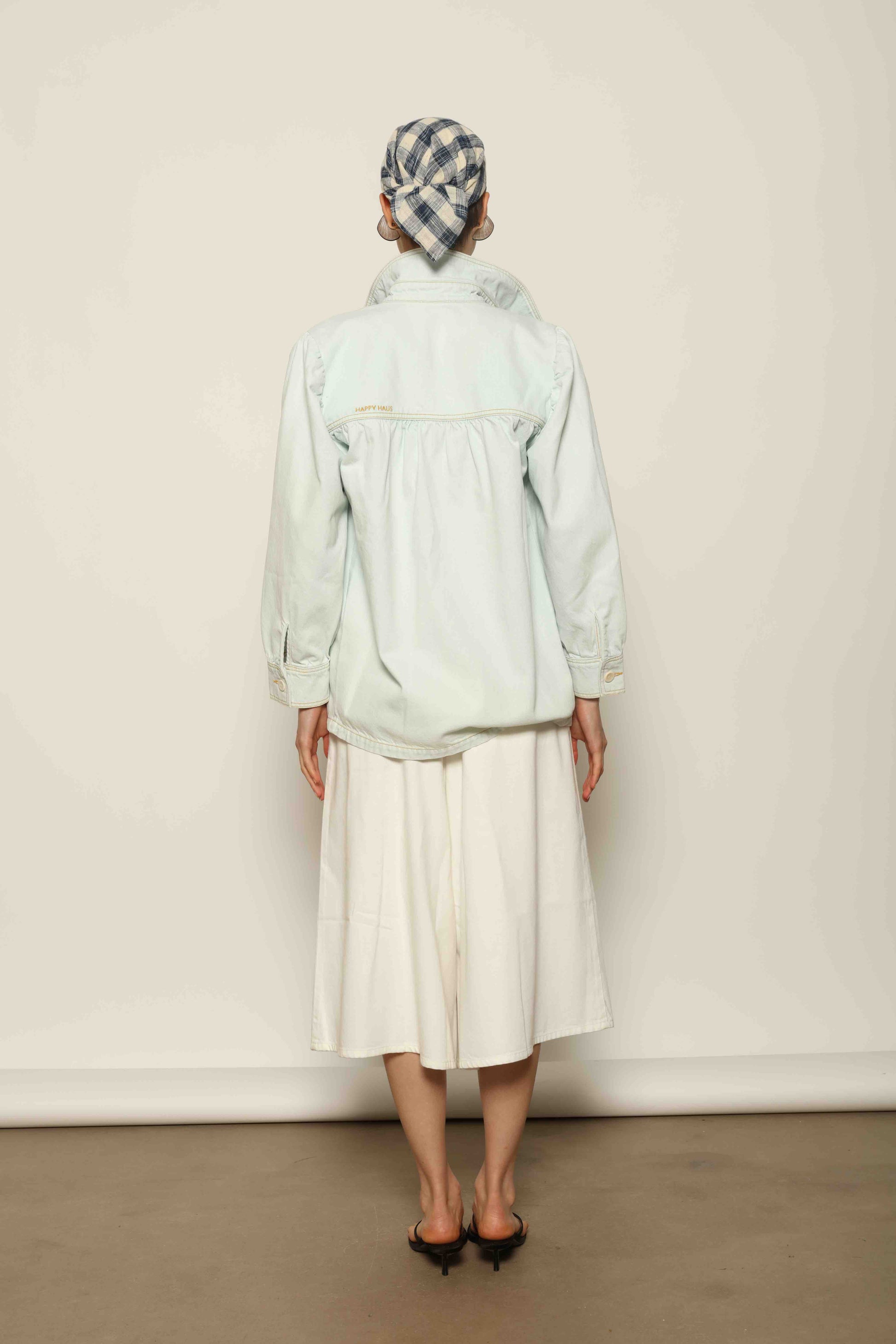 Model wearing the La Veste Peintre in Summer Blue by Happy Haus from the House of Nomad Stories collection, featuring a relaxed fit, light blue denim, patch pockets, wooden button closure, and workwear-inspired design.