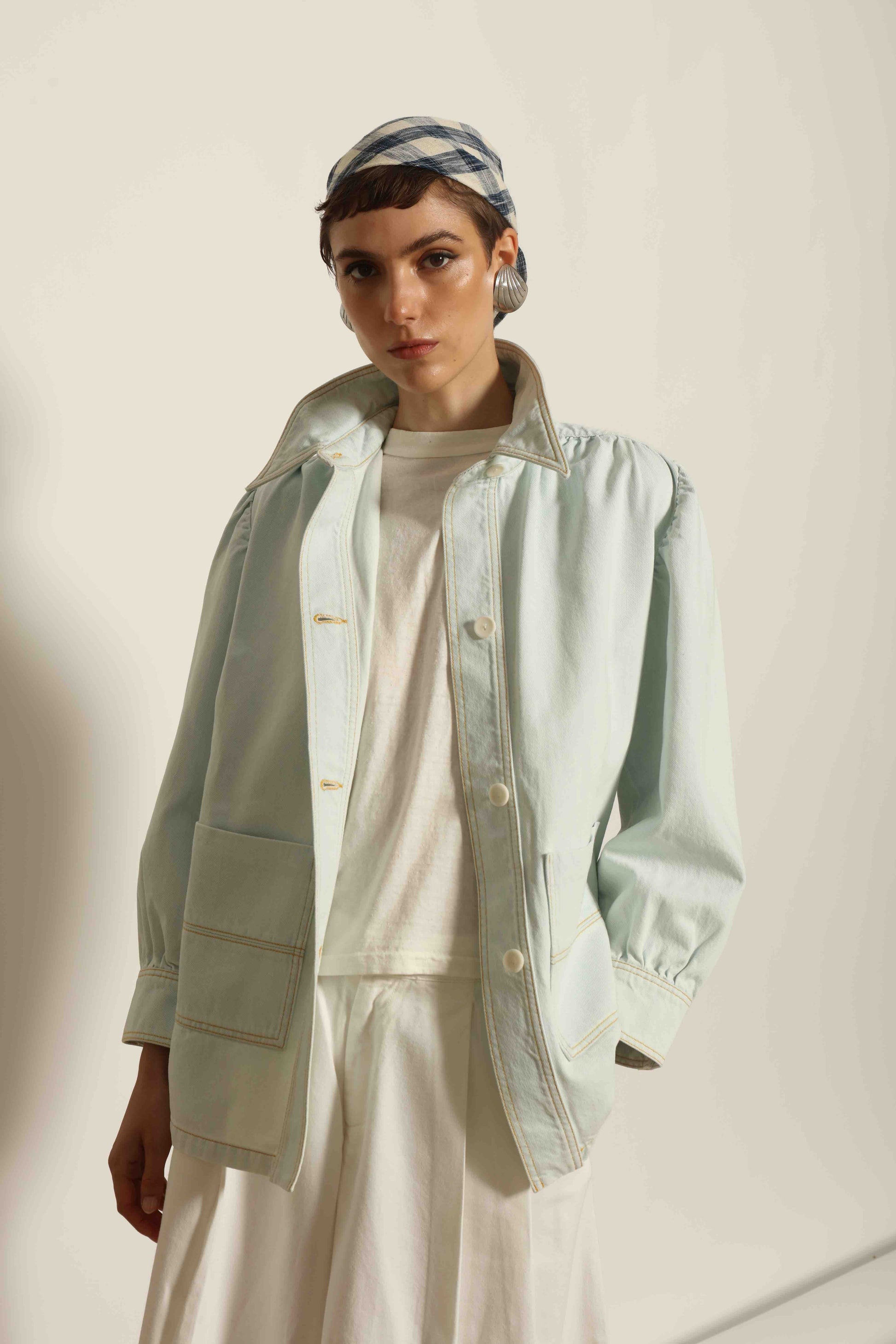 Model wearing the La Veste Peintre in Summer Blue by Happy Haus from the House of Nomad Stories collection, featuring a relaxed fit, light blue denim, patch pockets, wooden button closure, and workwear-inspired design.