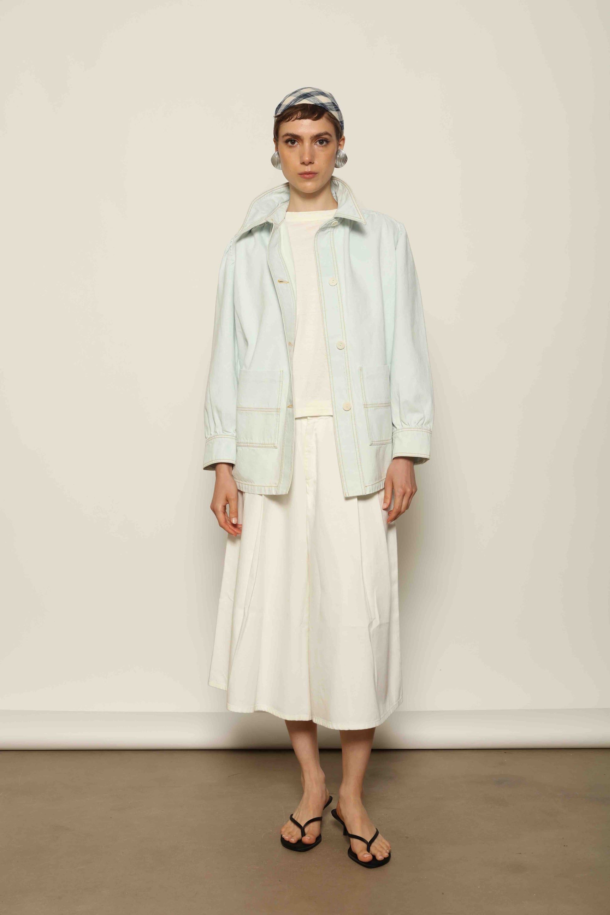 Model wearing the La Veste Peintre in Summer Blue by Happy Haus from the House of Nomad Stories collection, featuring a relaxed fit, light blue denim, patch pockets, wooden button closure, and workwear-inspired design.
