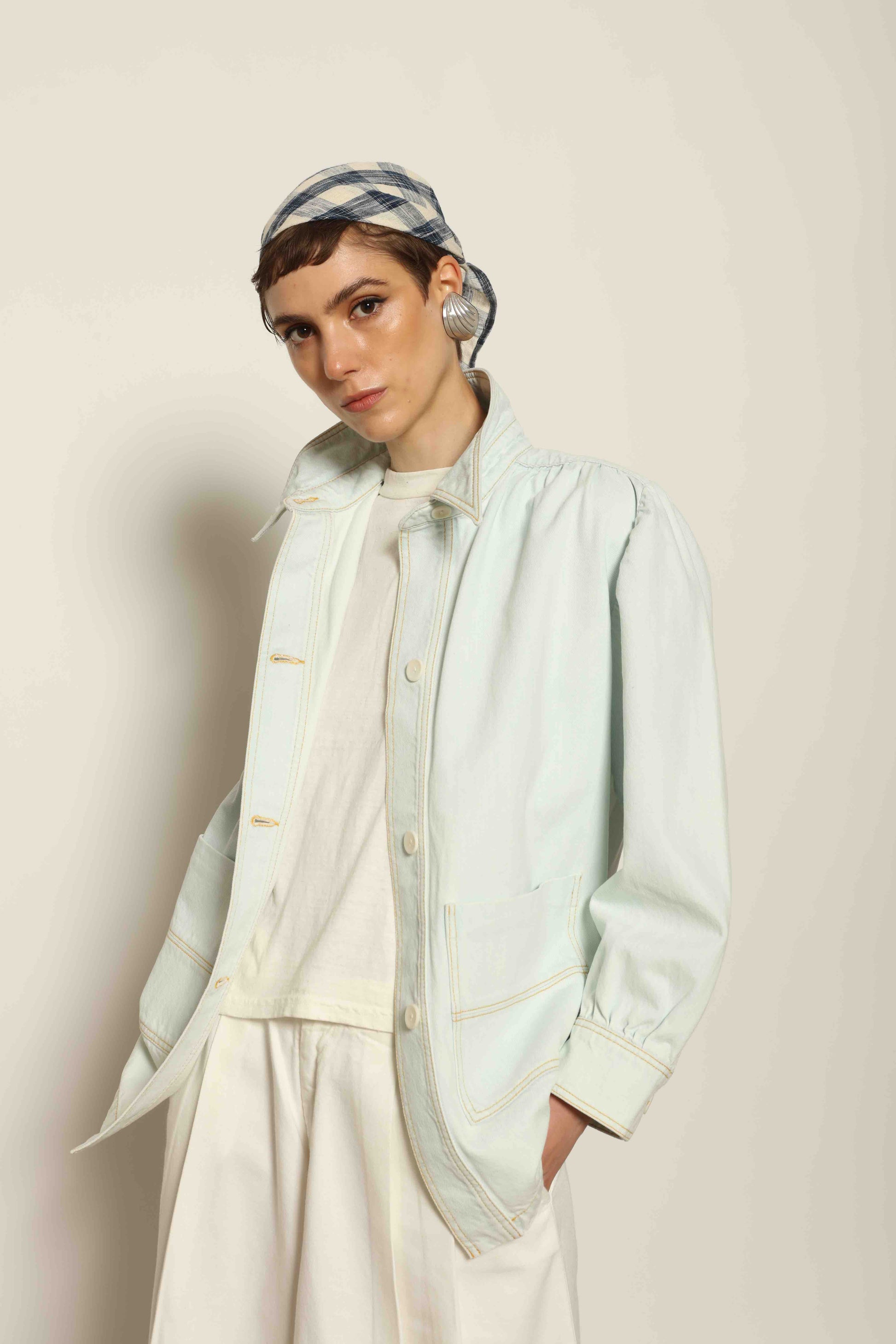 Model wearing the La Veste Peintre in Summer Blue by Happy Haus from the House of Nomad Stories collection, featuring a relaxed fit, light blue denim, patch pockets, wooden button closure, and workwear-inspired design.