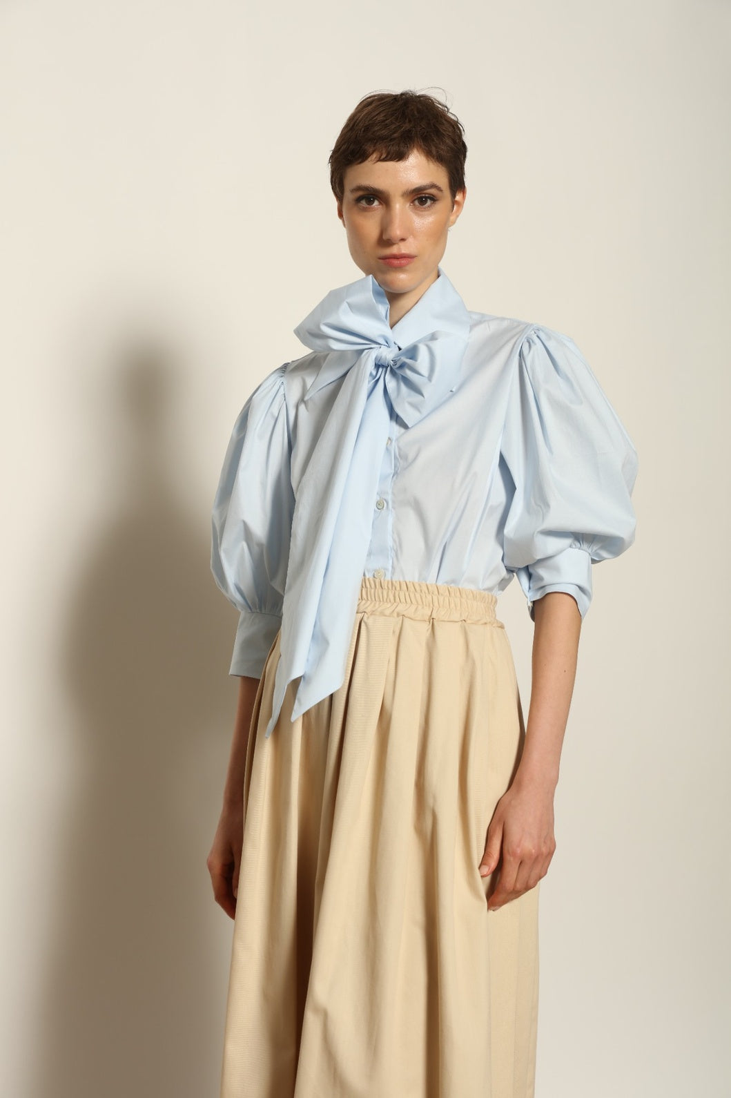 Model wearing the Karin Sky Blue Short Sleeves Blouse by House of Nomad Stories, featuring organic cotton fabric, sculptural balloon sleeves, structured silhouette, and a versatile neck tie detail.